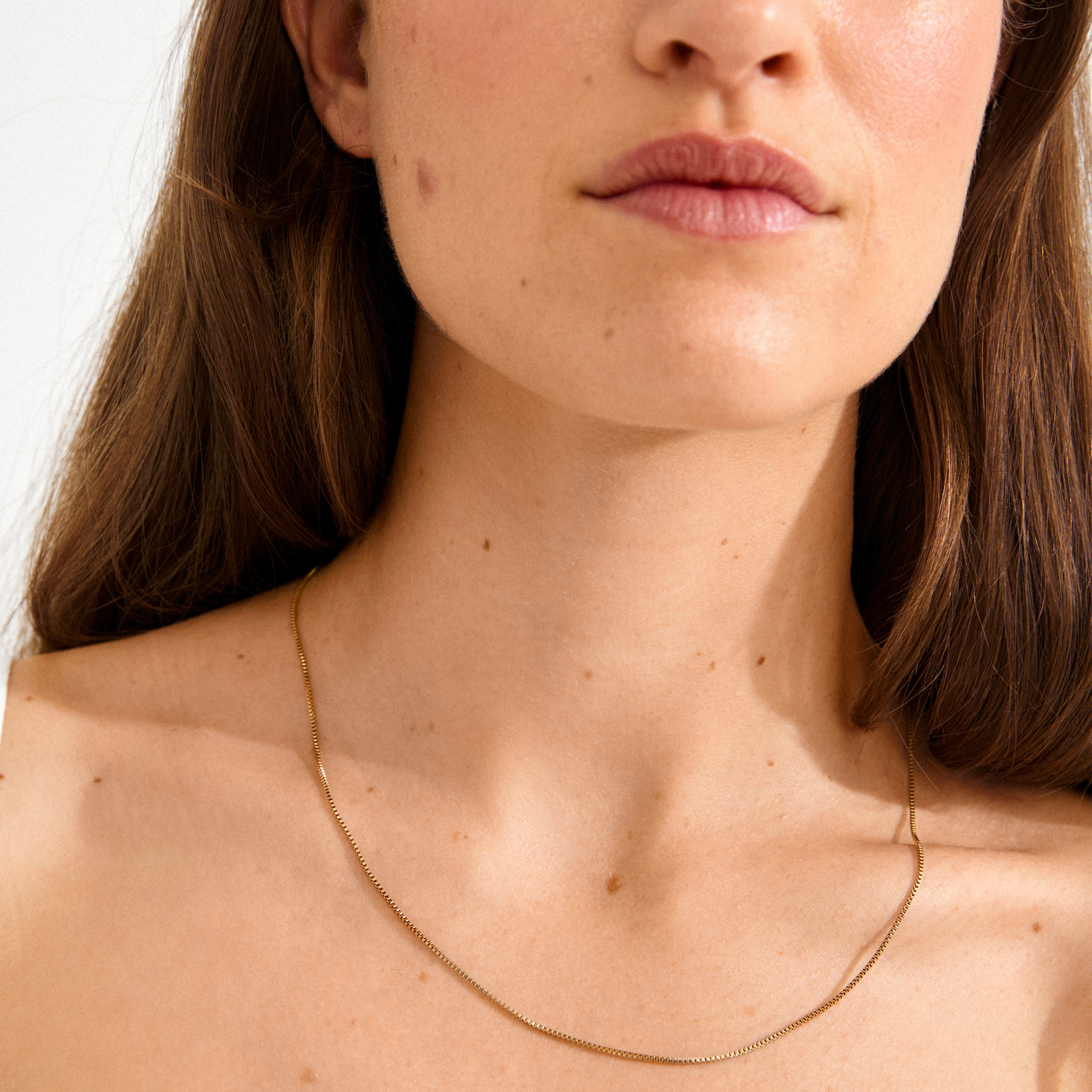Close-up of a woman's neck wearing the NANCY necklace, a 50 cm gold-plated venetian chain by Pilgrim, elegantly draping along her collarbones.