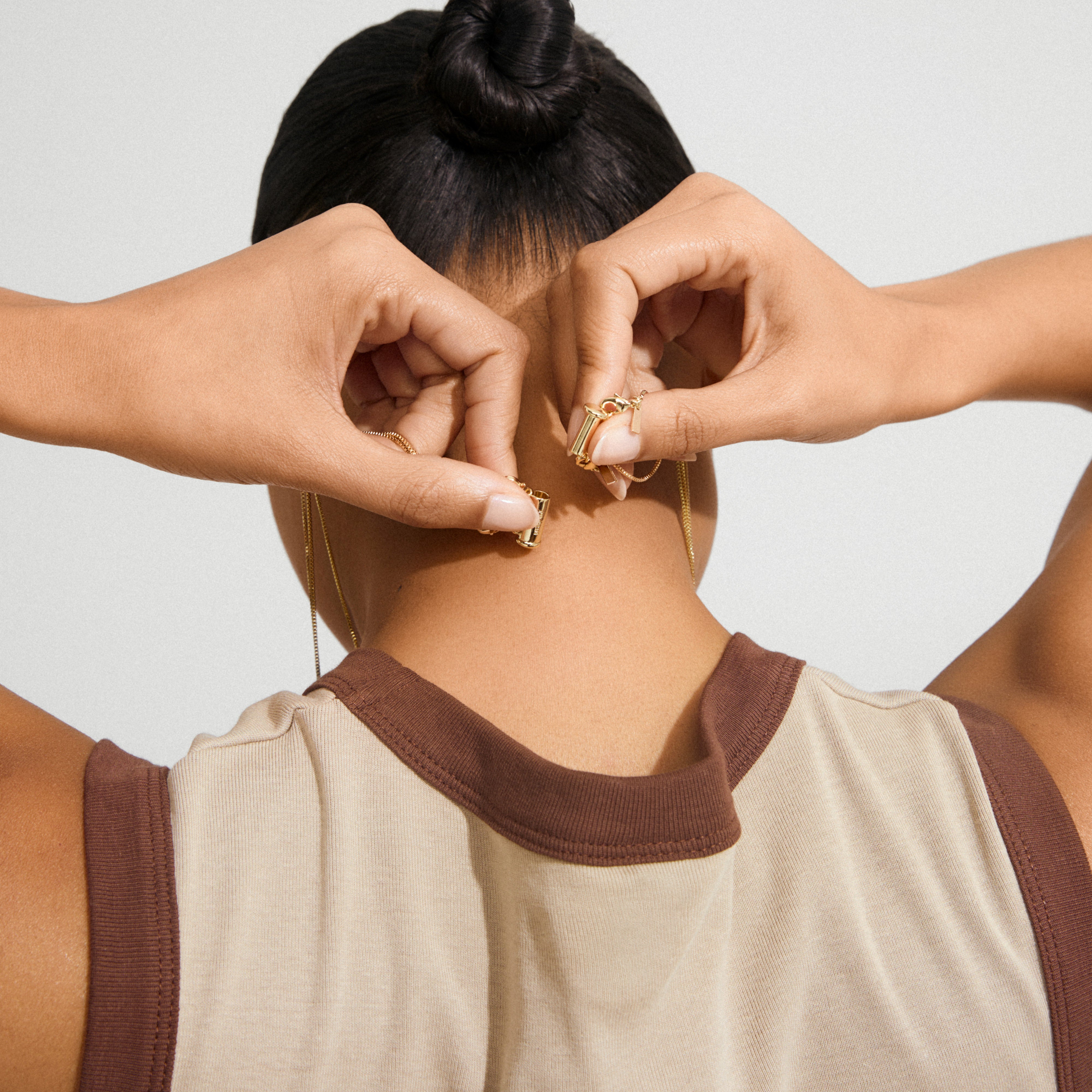 A person adjusts the clasp of the 50 cm gold-plated NANCY necklace, showcasing its simplicity and elegance as a versatile accessory.