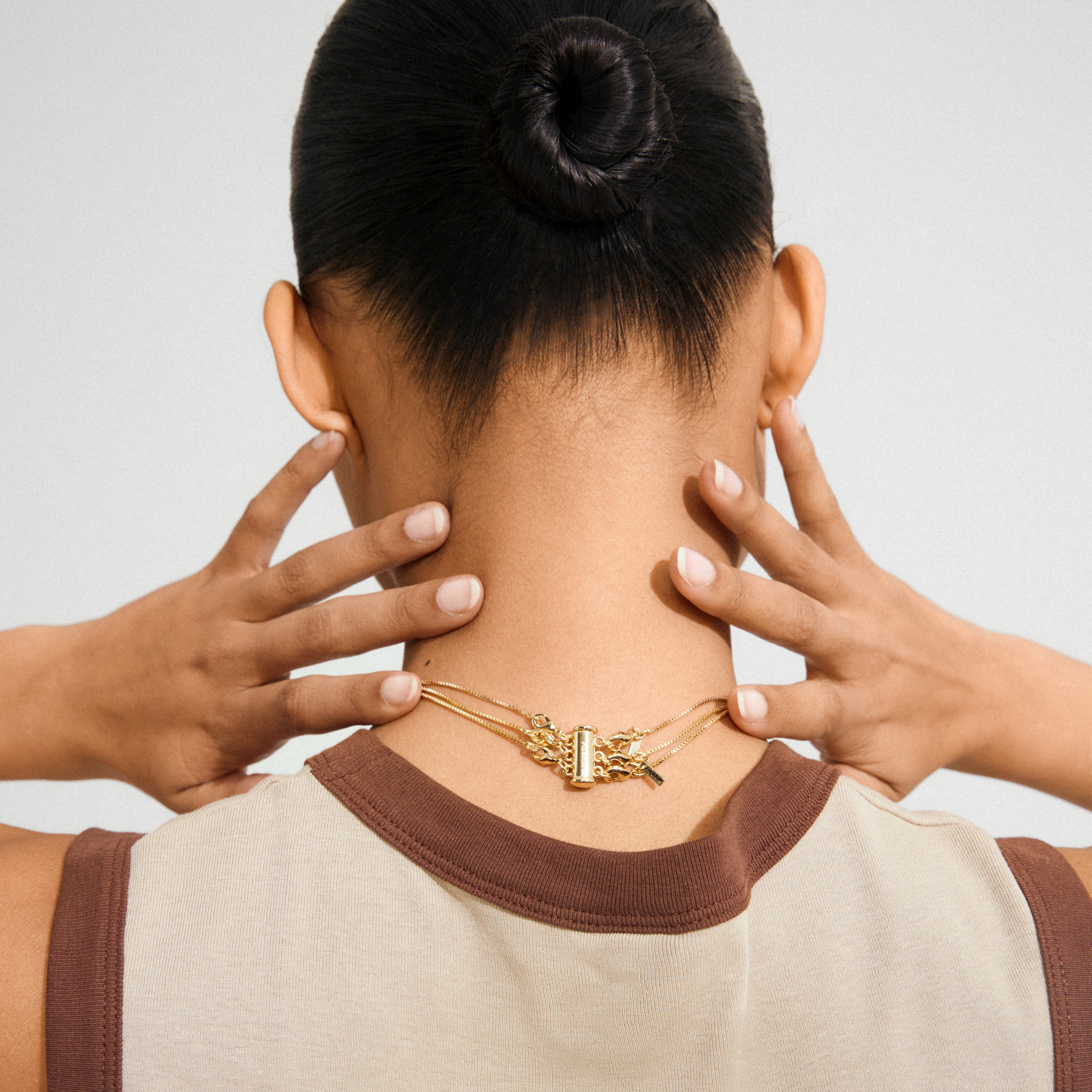 Person with a neat bun shows the NANCY necklace 50 cm gold-plated, clasp visible at the nape, styled for versatile, minimalist elegance.