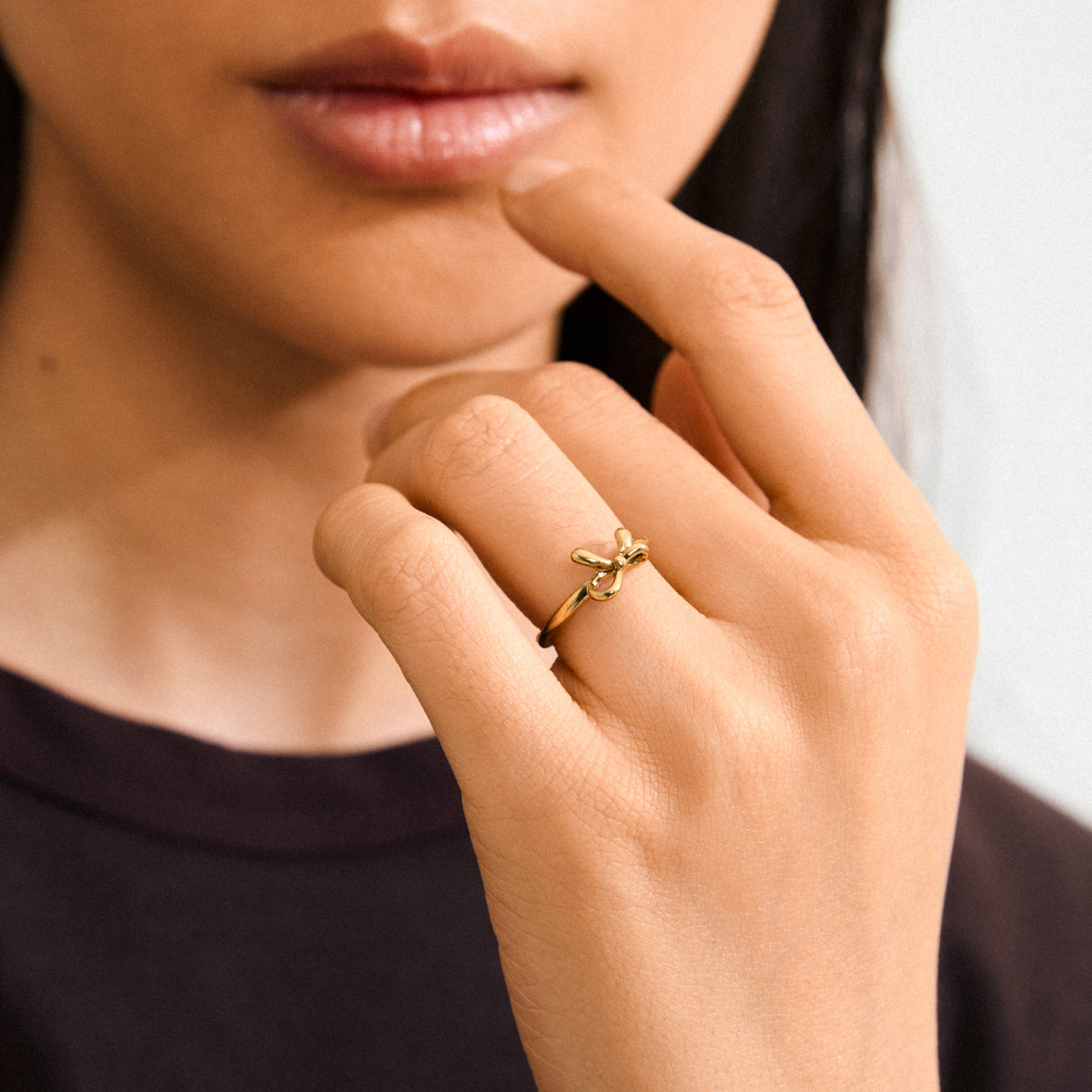 Close-up of a woman's hand wearing the LULU bow stack ring, gold-plated, showcasing its sleek, romantic design from Pilgrim's Lulu collection.