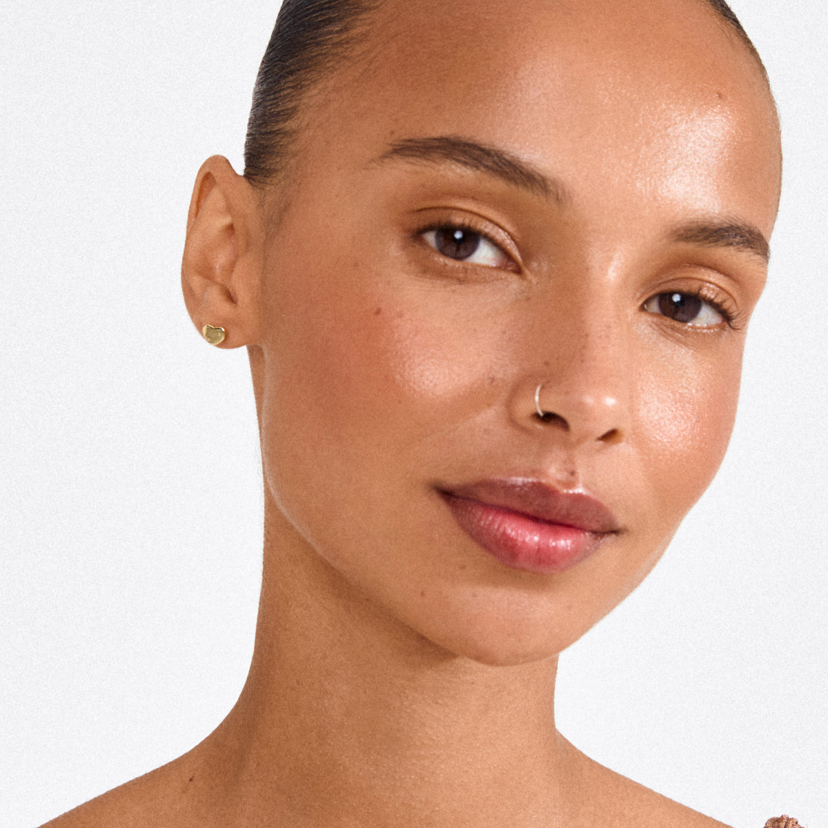Close-up of a woman wearing Pilgrim's ARIN gold-plated heart-shaped stud earring, showcasing its elegant, minimalist design with a subtle romantic touch.