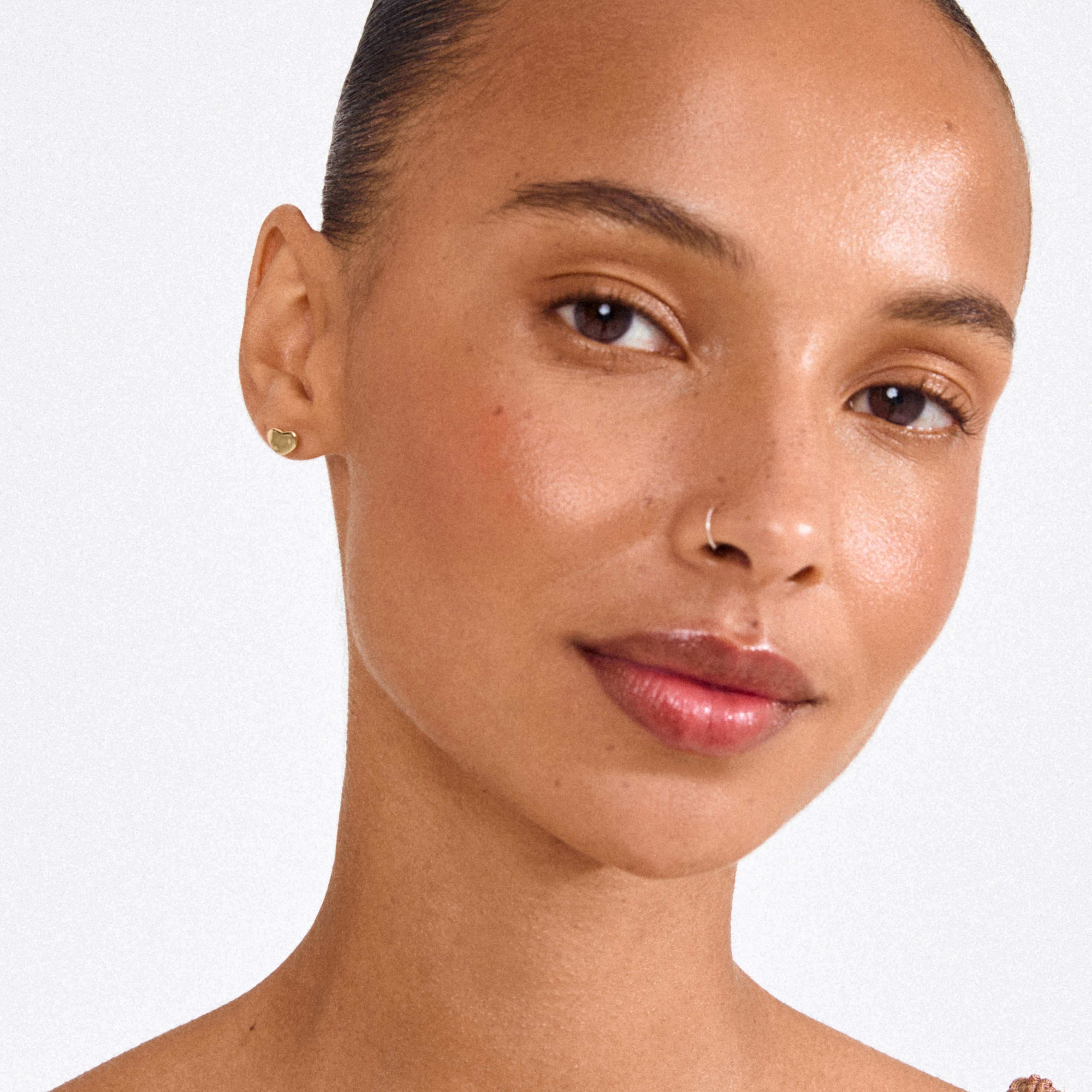 Close-up of a woman wearing Pilgrim's ARIN gold-plated heart-shaped stud earring, showcasing its elegant, minimalist design with a subtle romantic touch.