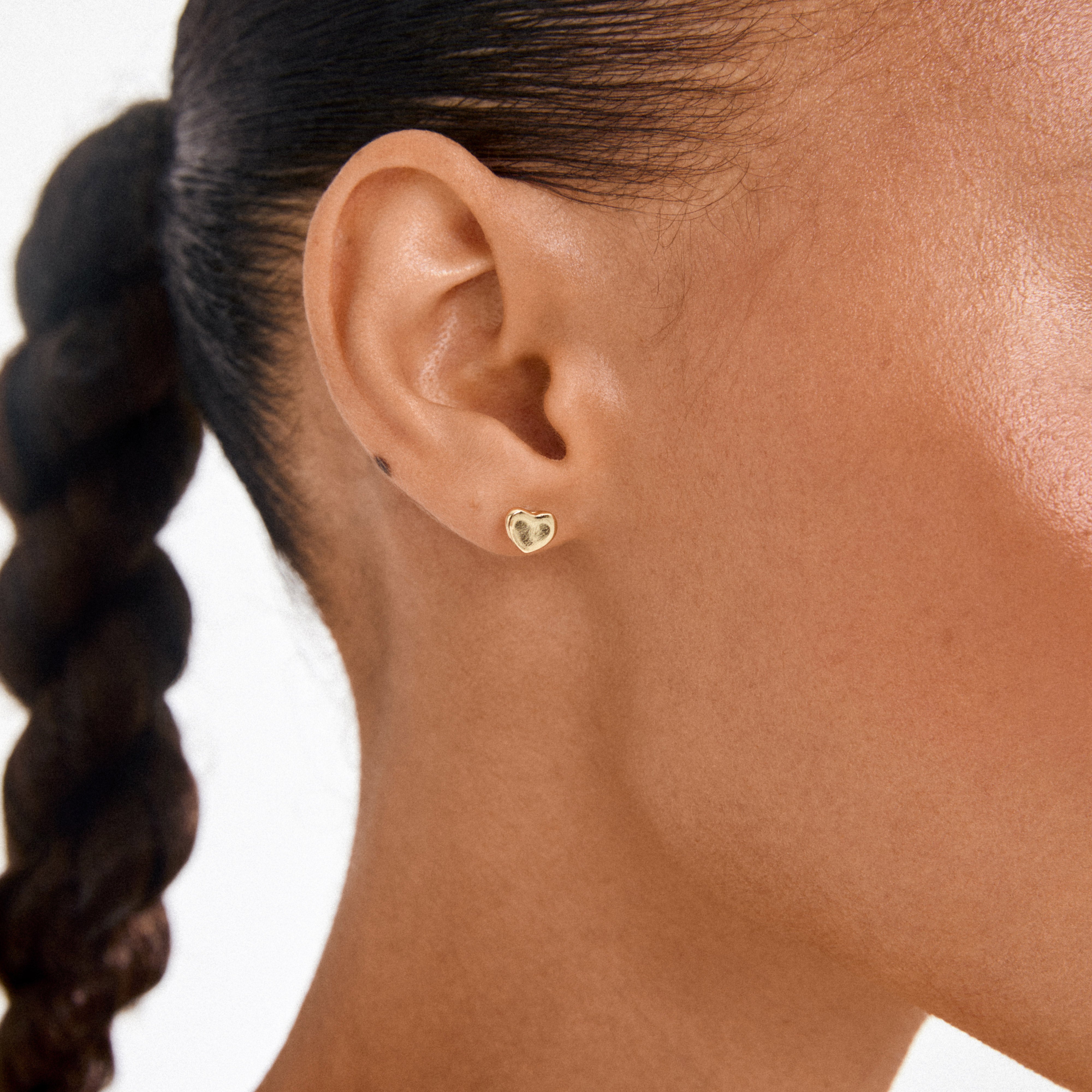 Close-up of ARIN gold-plated heart-shaped stud earring on earlobe, showcasing its simple, romantic design with a touch of elegance.