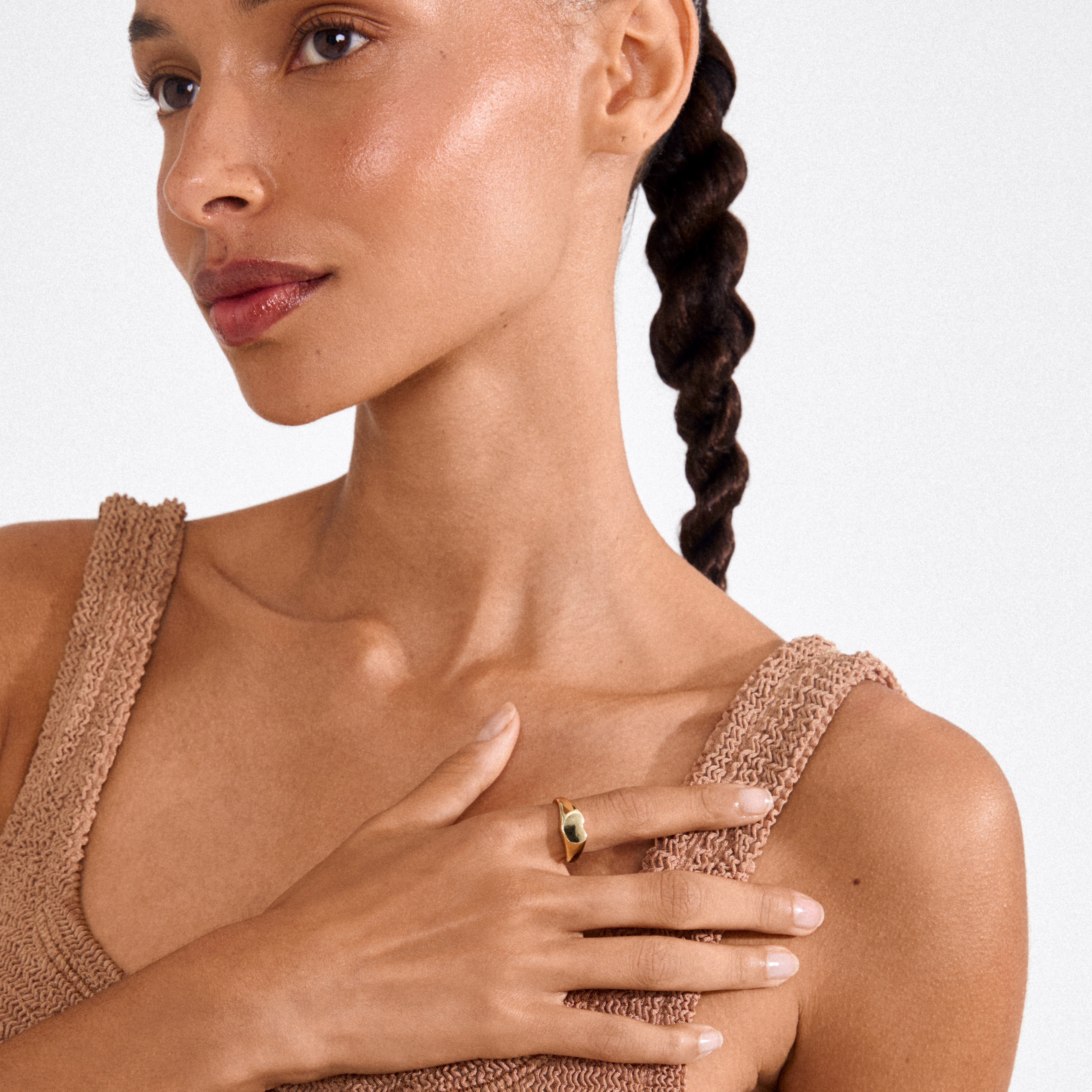 Close-up of woman wearing Pilgrim's ARIN gold-plated ring, showcasing its minimalist signet style with a heart, elegantly paired with a neutral knitted top.