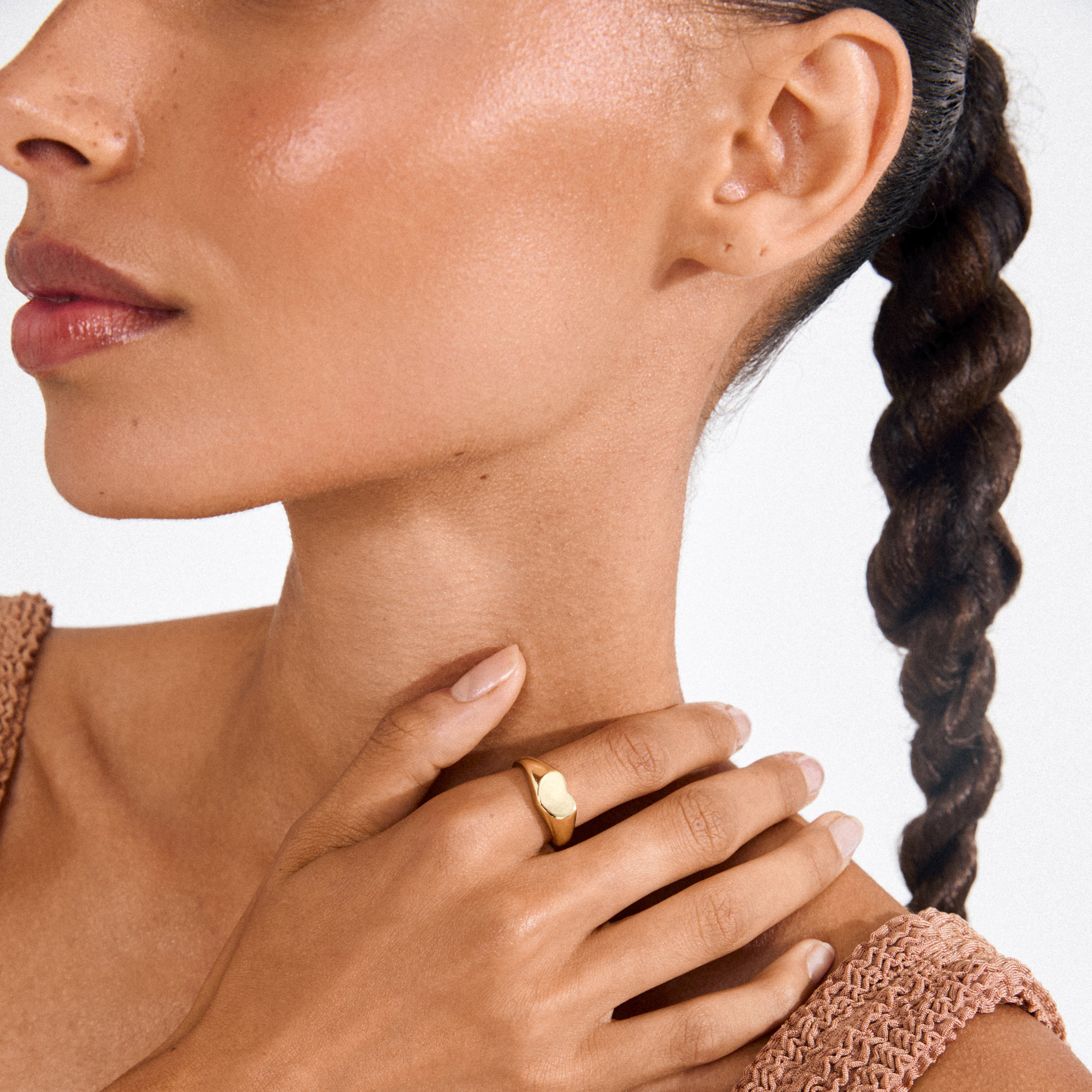 Woman wearing Pilgrim's ARIN gold-plated signet ring with a minimalist heart design, resting on her collarbone, paired with a sleeveless knit top.