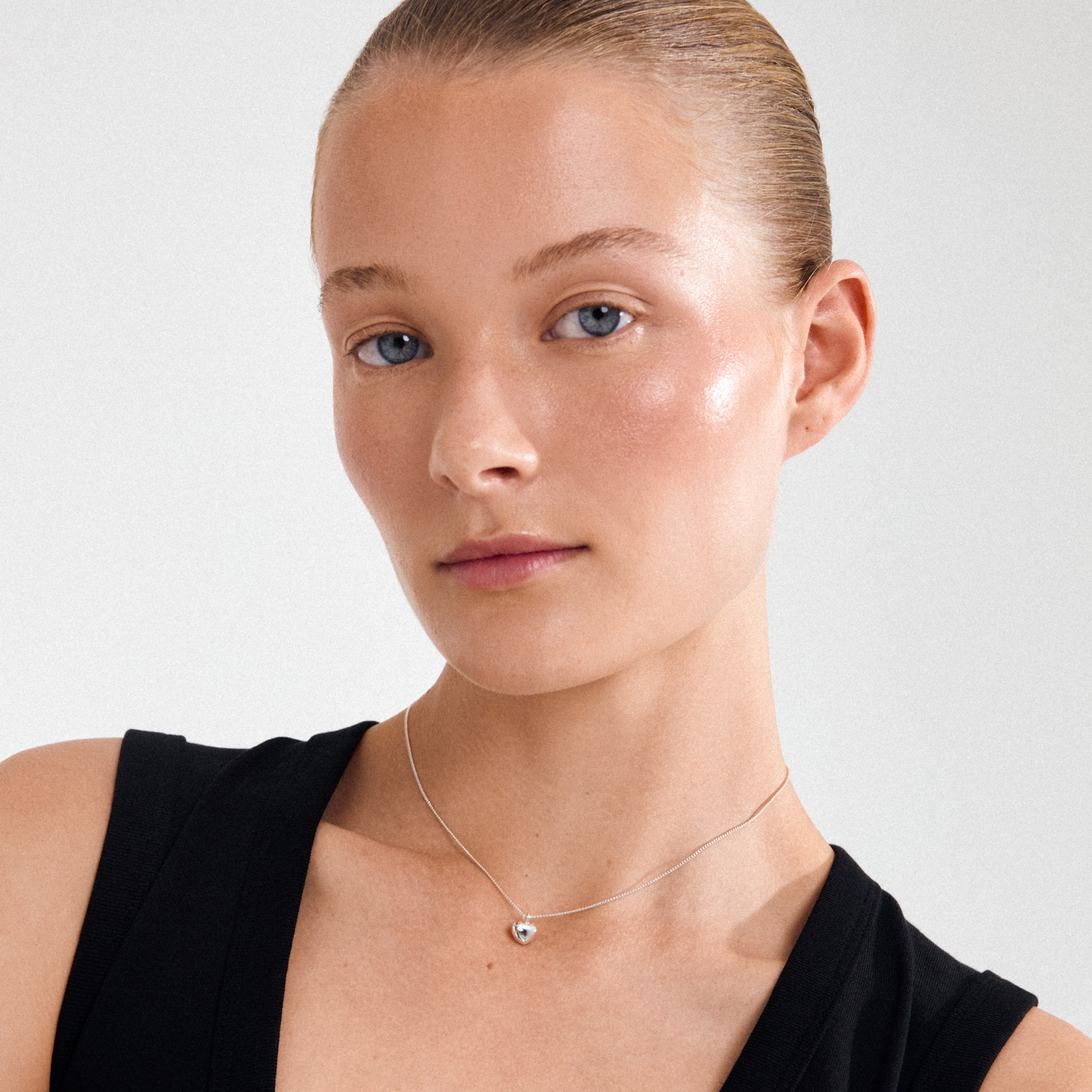 Young woman wearing Pilgrim's ARIN silver-plated necklace, featuring a fine chain and small heart pendant, highlighting minimalist elegance and understated style.
