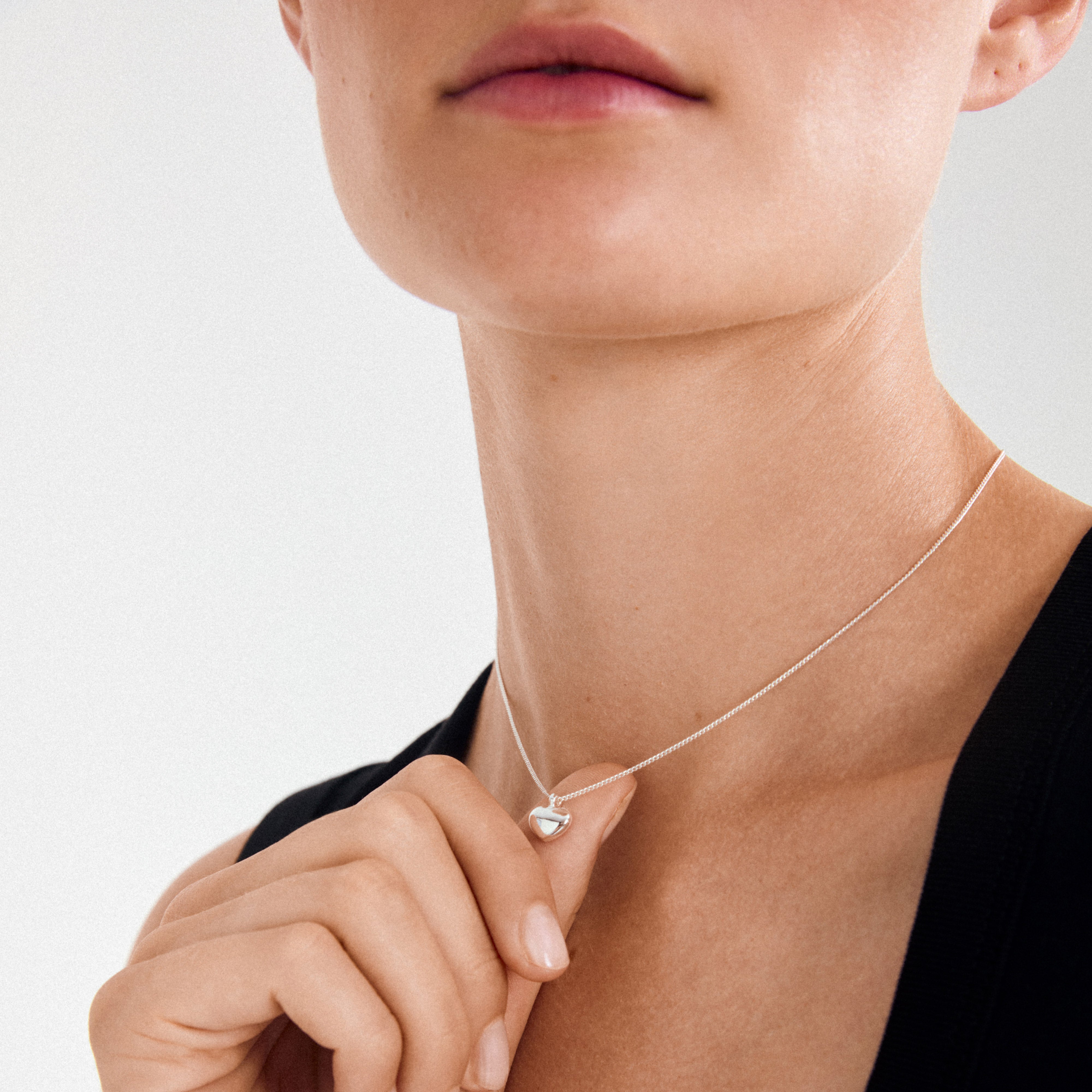 Close-up of ARIN silver-plated necklace with a heart-shaped pendant, held gently. A simple yet striking piece, perfect for everyday wear.