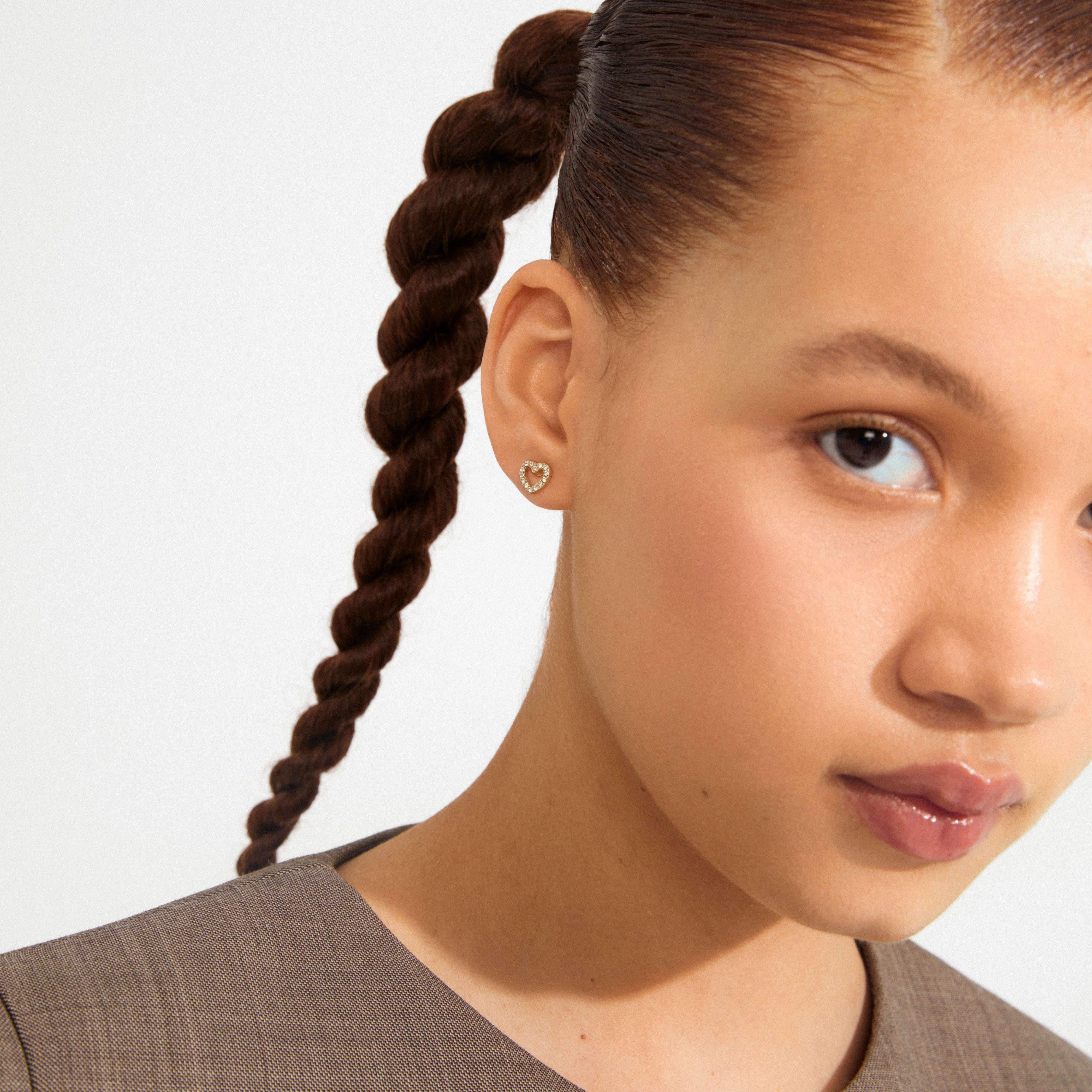 Young woman wearing EDIE crystal heart earrings, gold-plated, with tiny sparkling stones, adding a touch of glam and romance to her chic, minimalist look.