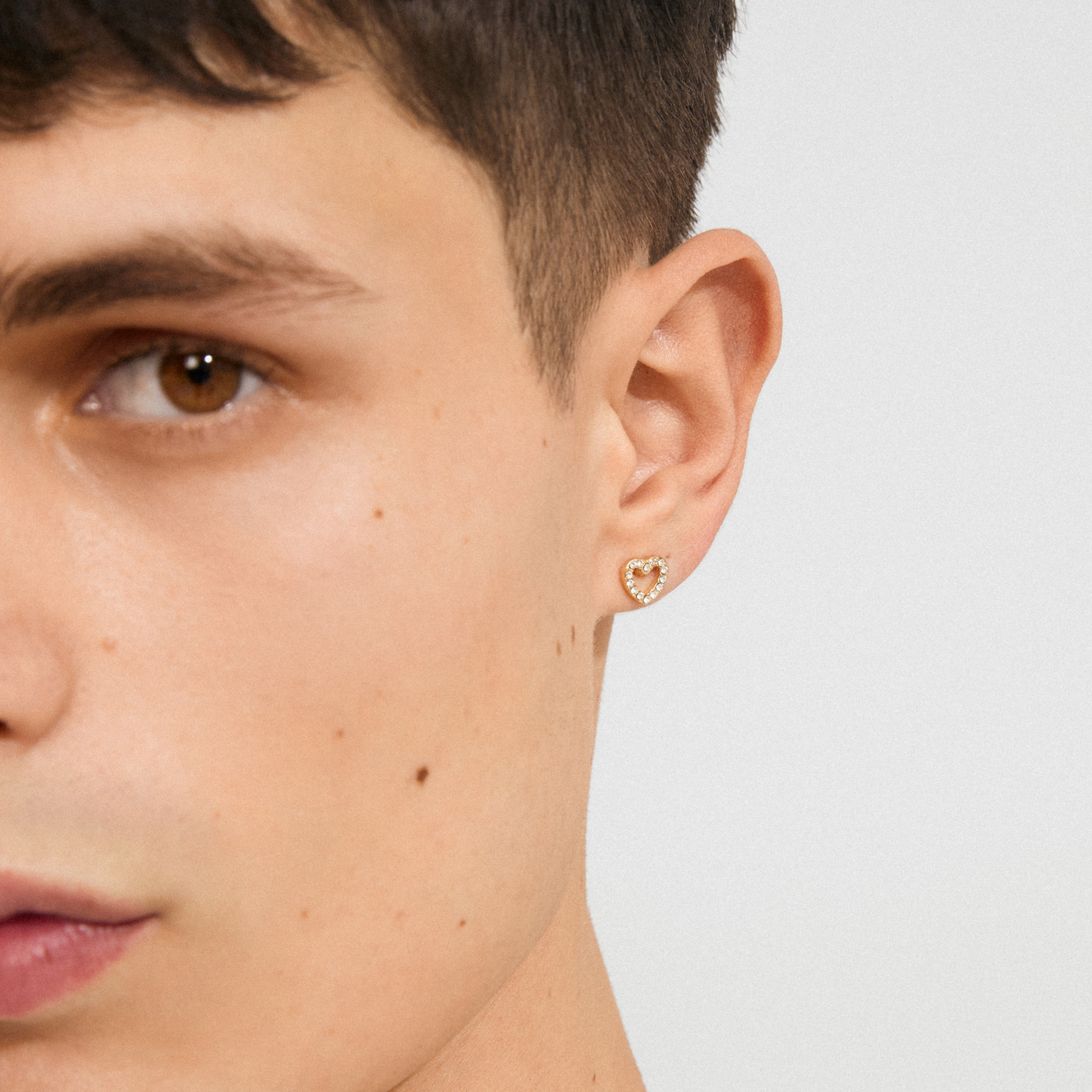 EDIE crystal heart earrings gold-plated, featuring tiny sparkling stones on a young person's ear, showcasing delicate glam with a romantic touch.
