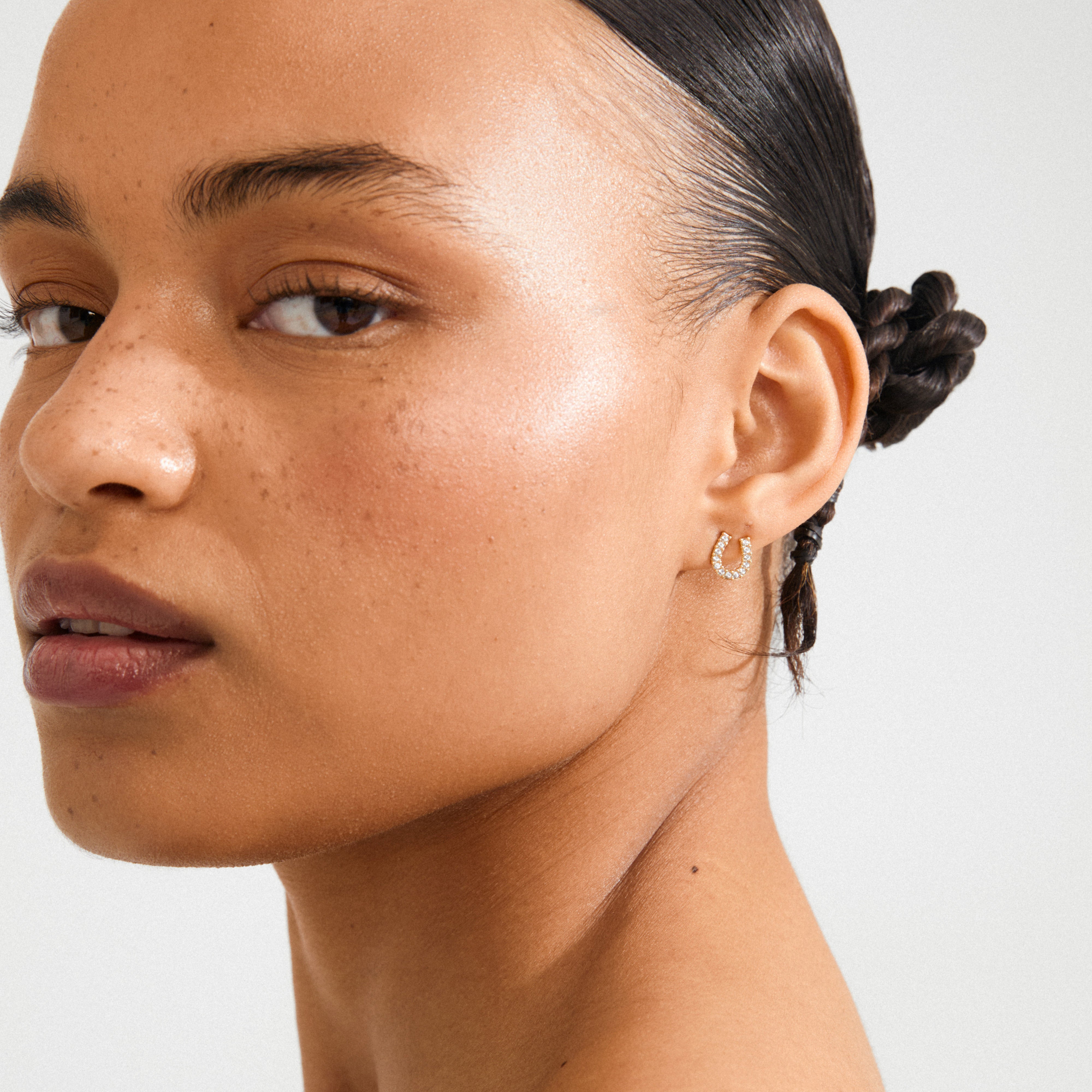 Close-up of a person wearing LEANNA good luck crystal earrings gold-plated, featuring sparkling crystals on a polished horseshoe design, symbolizing good luck.