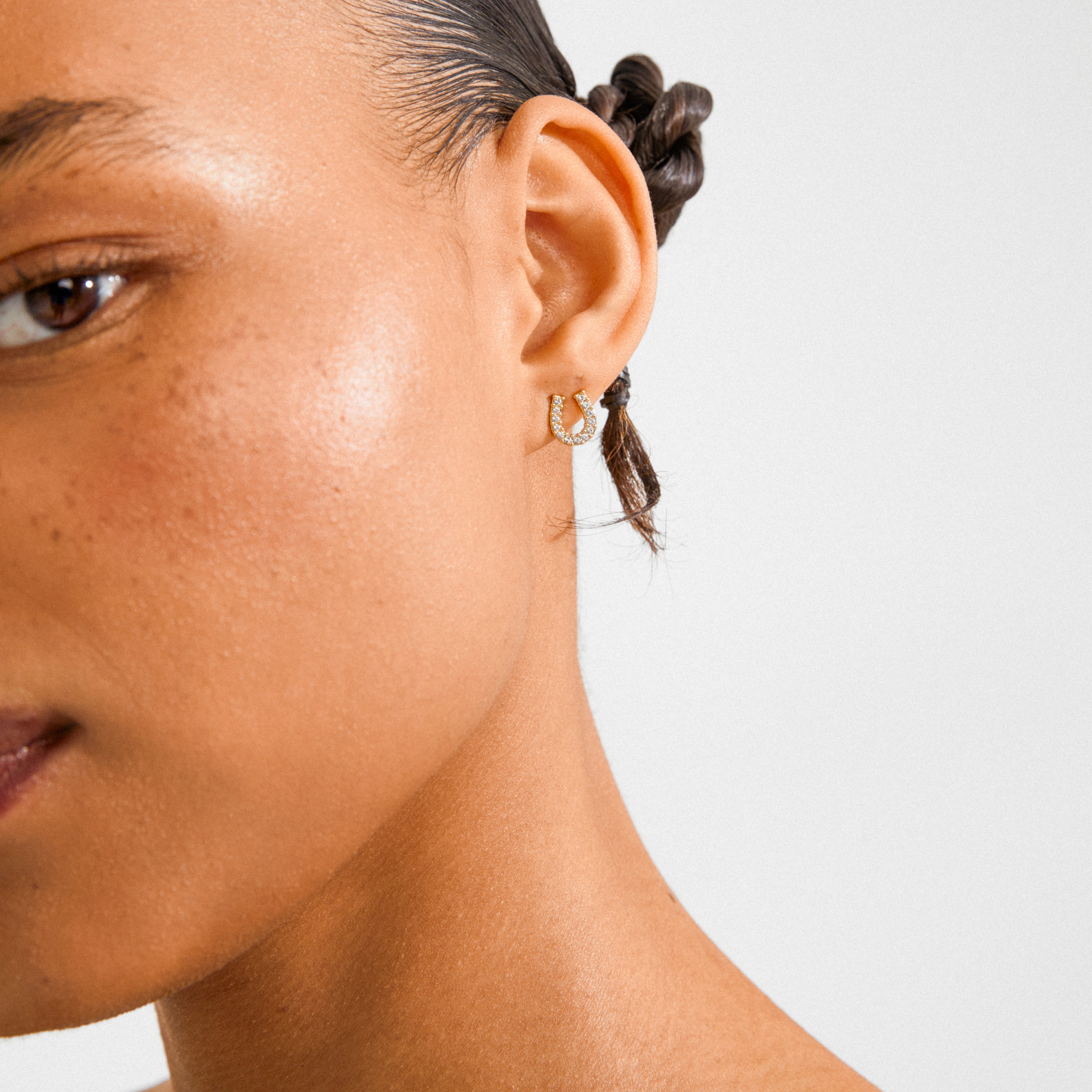 Close-up of an ear wearing LEANNA good luck crystal earrings, gold-plated horseshoe hoops set with sparkling stones, embodying classic elegance and timeless design.