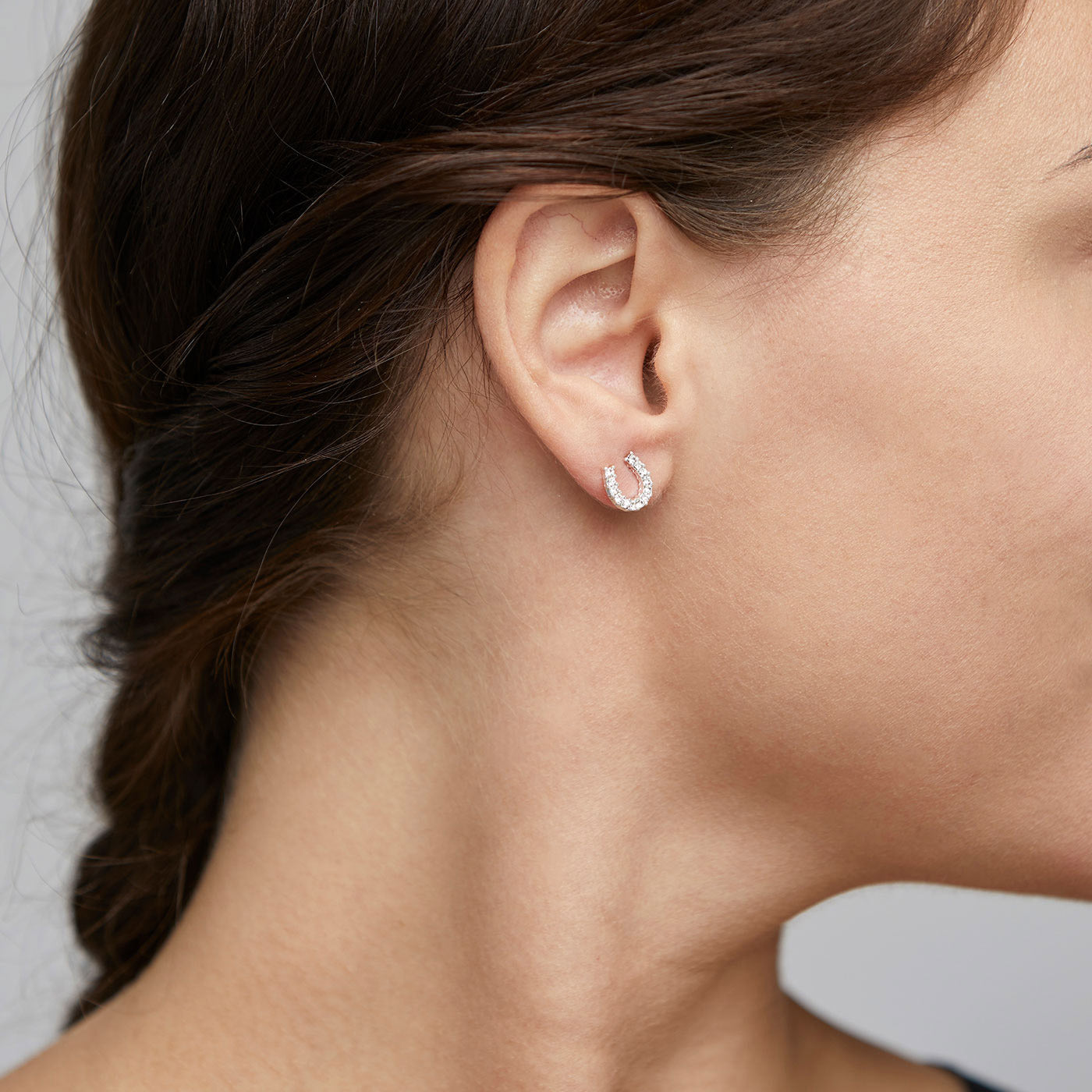LEANNA good luck crystal earrings, silver-plated, shown on a woman's ear. Horseshoe design with polished sides and crystal-studded top, capturing light beautifully.