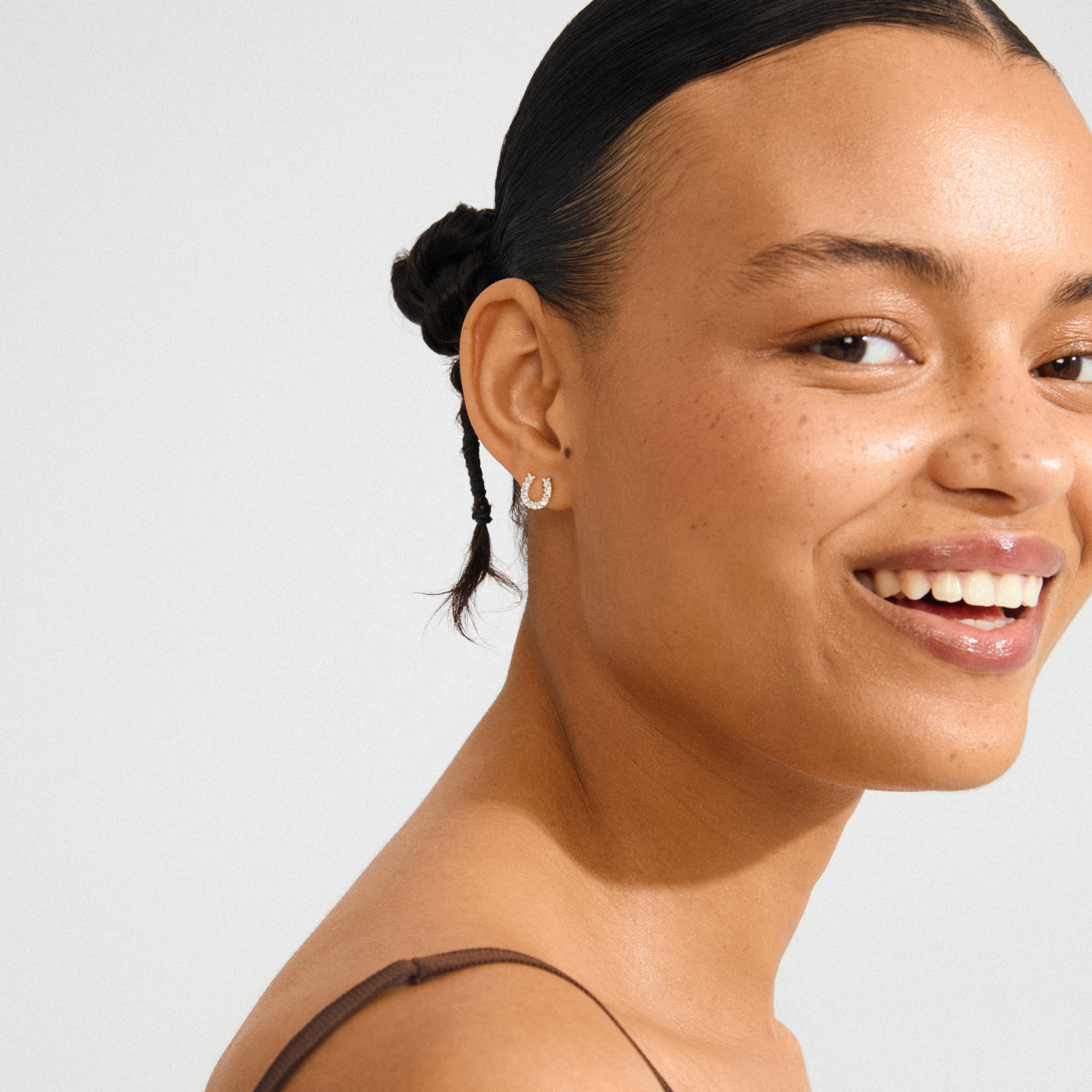 Young woman wearing LEANNA good luck crystal earrings, silver-plated horseshoe studs with sparkling crystals, styled to enhance natural beauty and capture light.