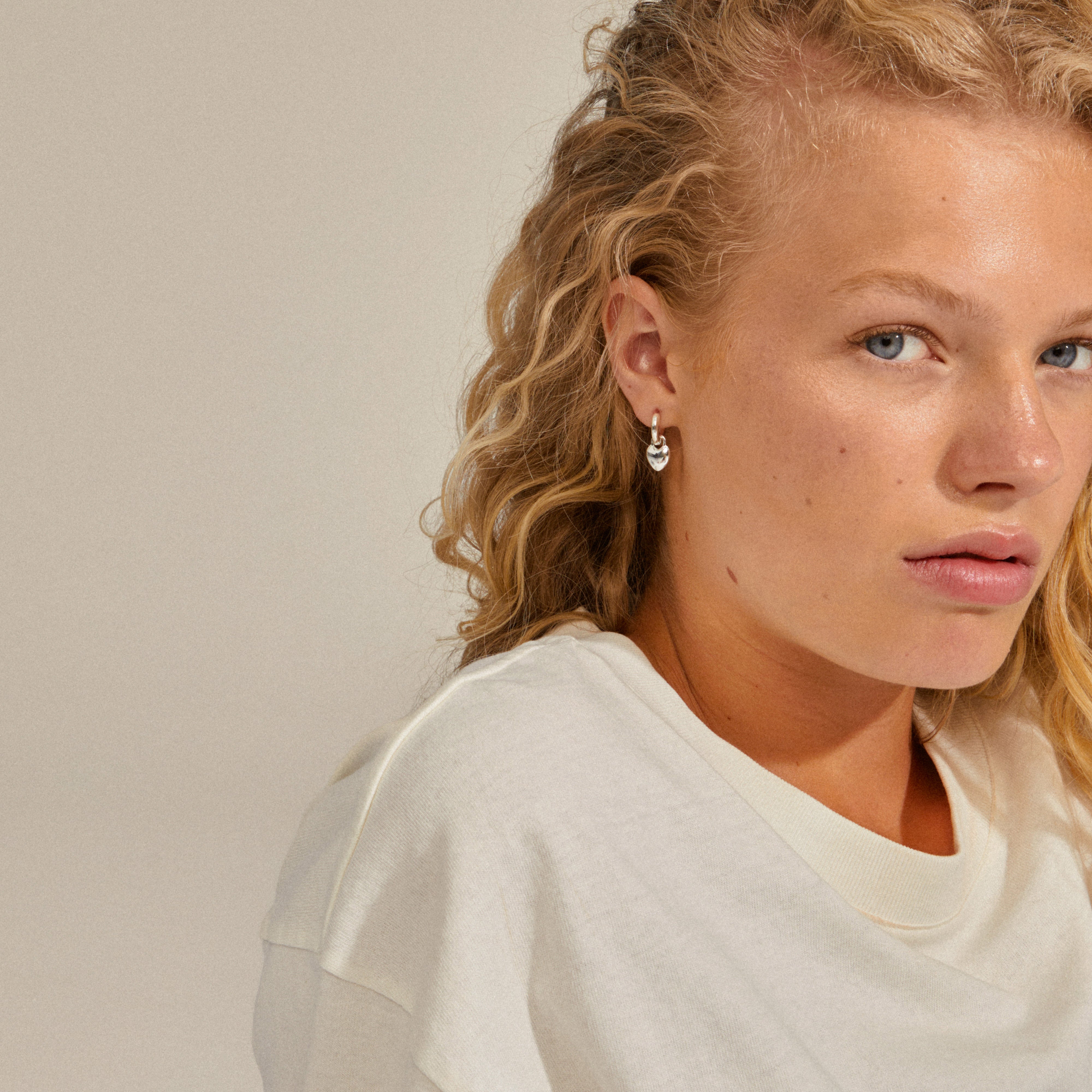 SOPHIA heart hoops silver-plated earrings worn by a woman, showcasing their elegant heart pendants that add subtle movement to enhance facial features.