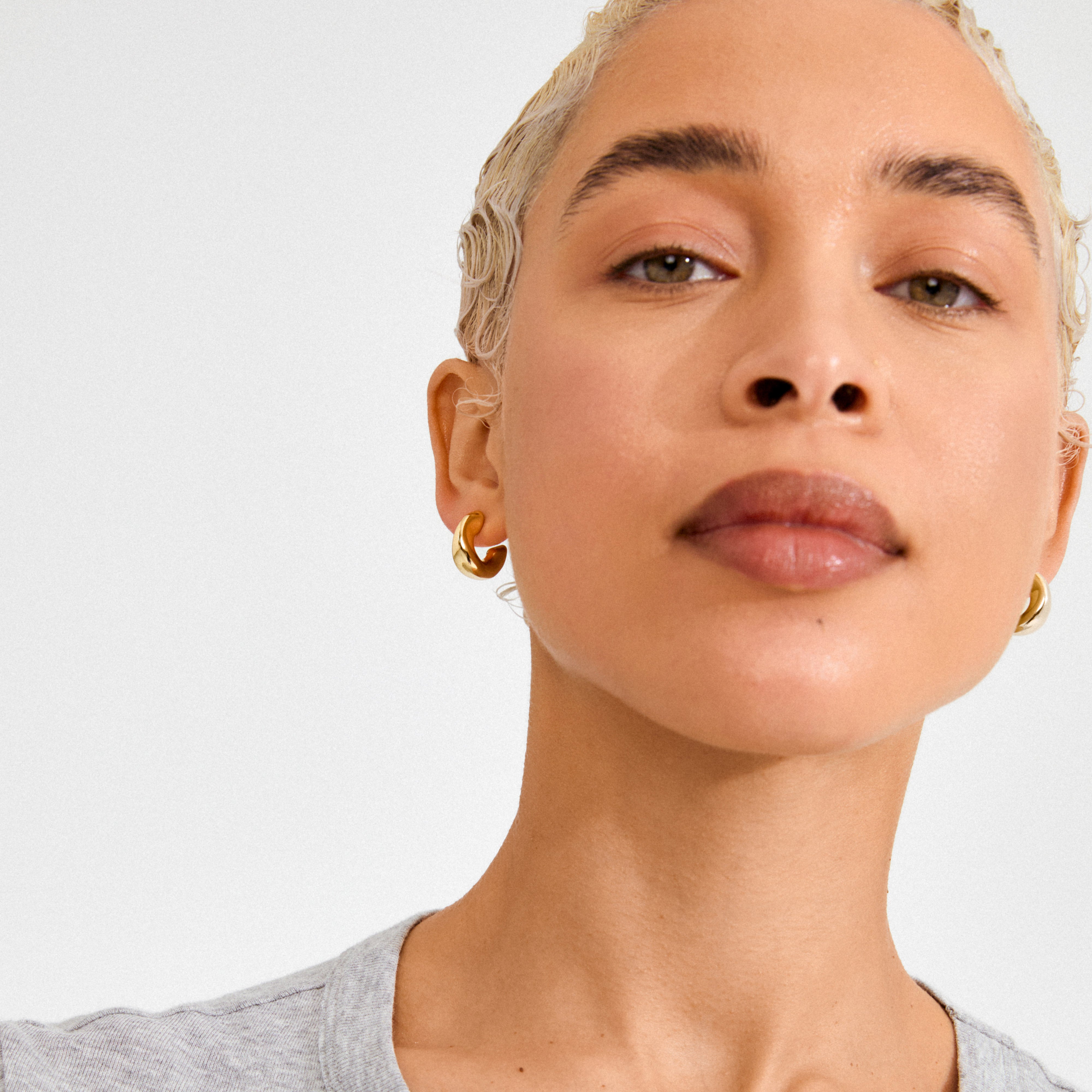 Person wearing JENNINGS gold-plated mini hoop earrings, showcasing their chunky, sculptural design that hugs the ear closely, embodying a chic and subtle statement.