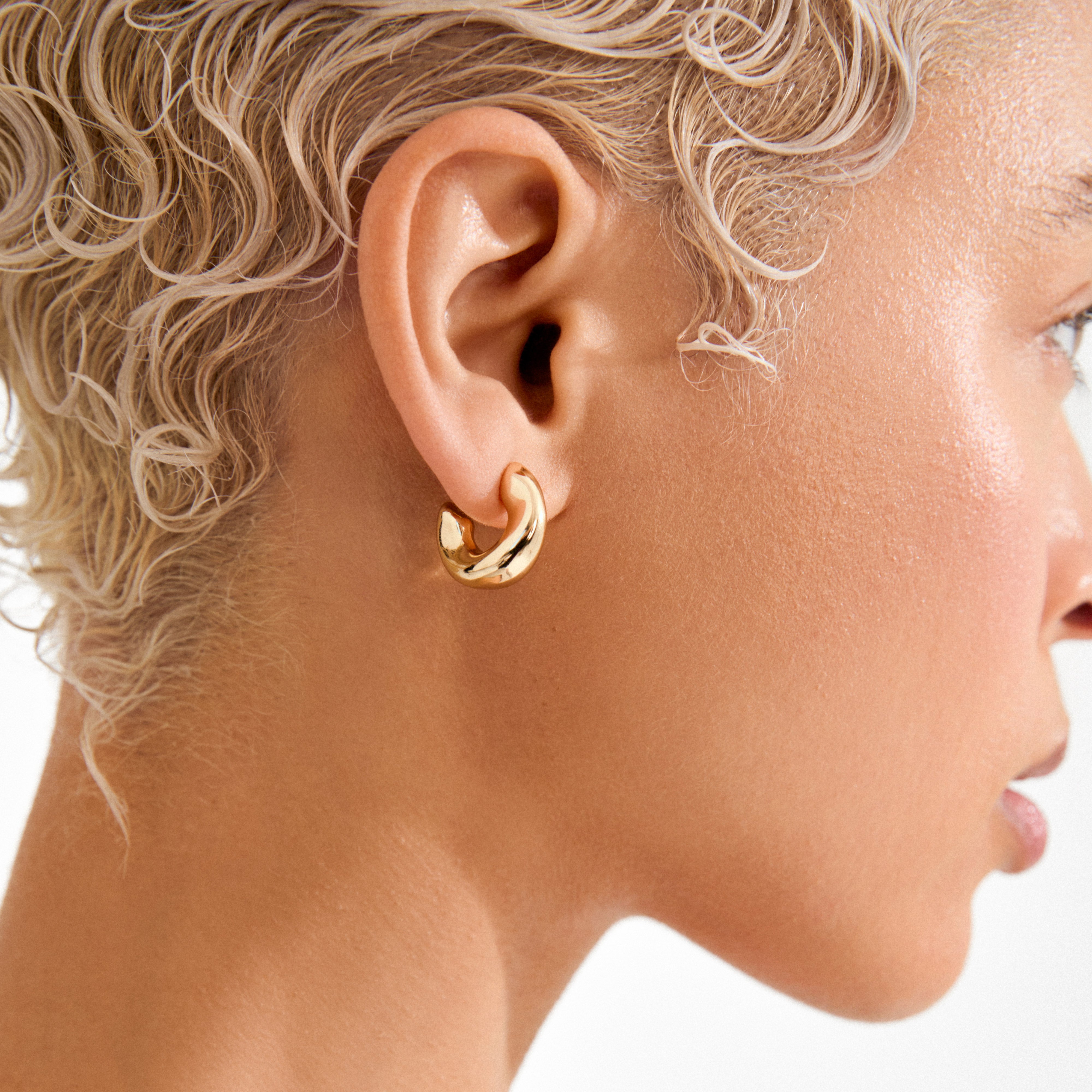 Person wearing JENNINGS gold-plated mini hoop earrings, showcasing their chunky, sculptural design that closely hugs the earlobe for a chic, effortless look.