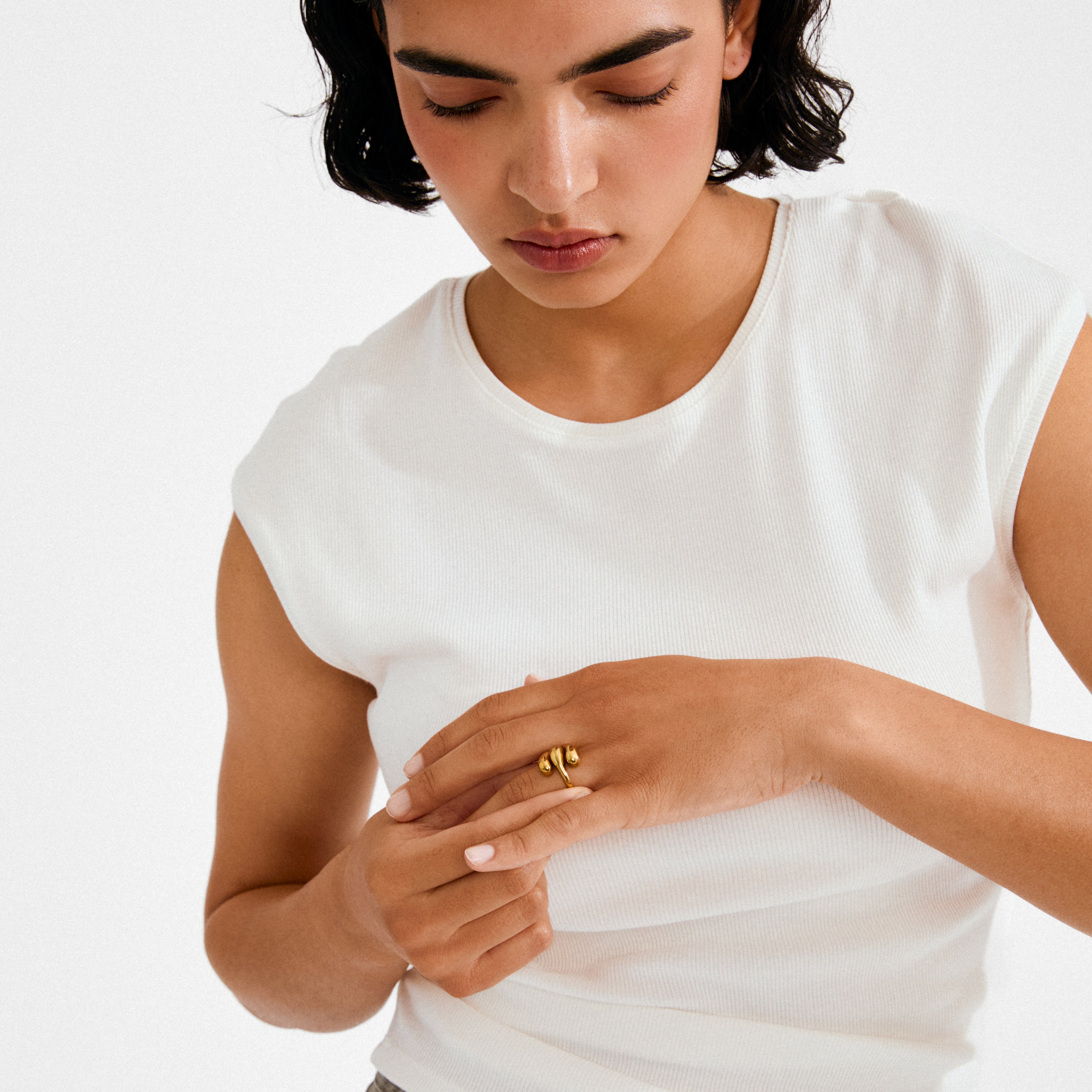 Young person wearing a white top highlights the gold-plated JENNINGS ring by Pilgrim, showcasing its sculptural, melting design on their finger.