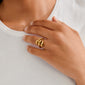 A hand wearing the gold-plated JENNINGS ring by Pilgrim, featuring three sculptural, droplet-like forms, resting on a rib-knit top.