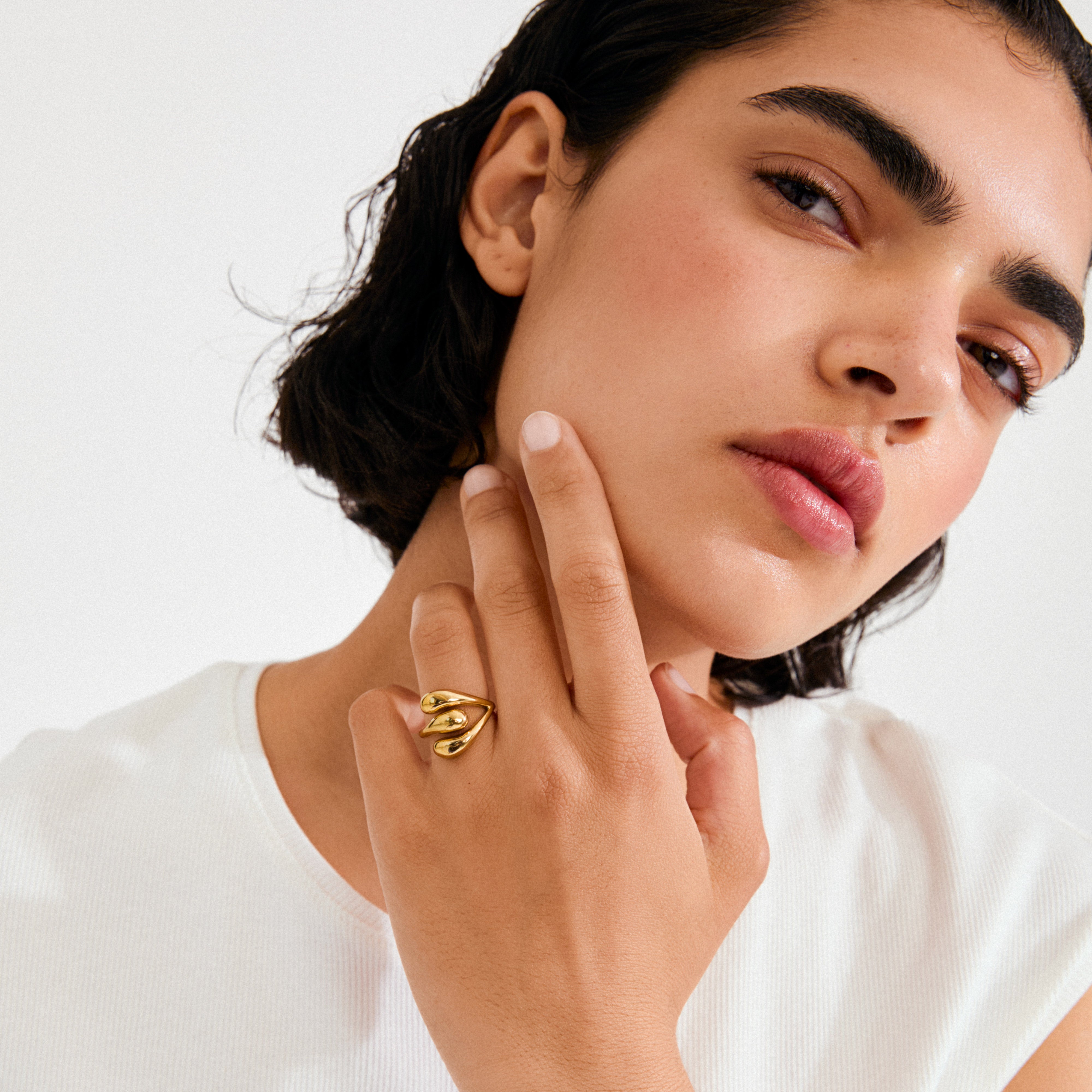 Young woman wearing the gold-plated JENNINGS ring with sculptural, looping design, accentuating her style. Soft lighting highlights the ring's polished finish and unique form.