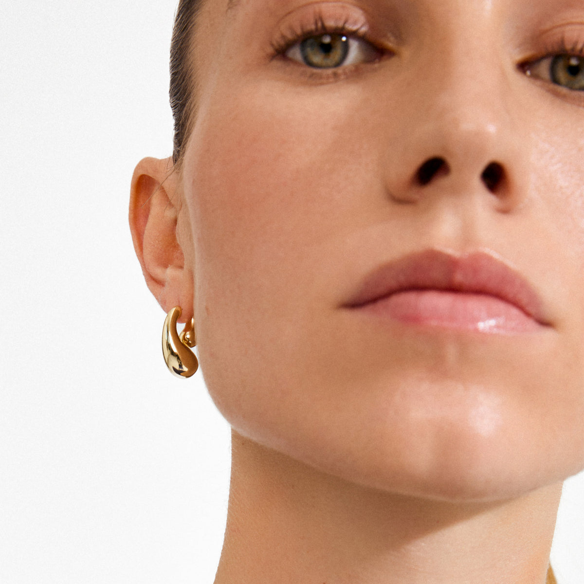 Close-up of a person's ear wearing gold-plated JENNINGS earrings by Pilgrim, showcasing a sculptural double drop design with a polished, liquid-like finish.