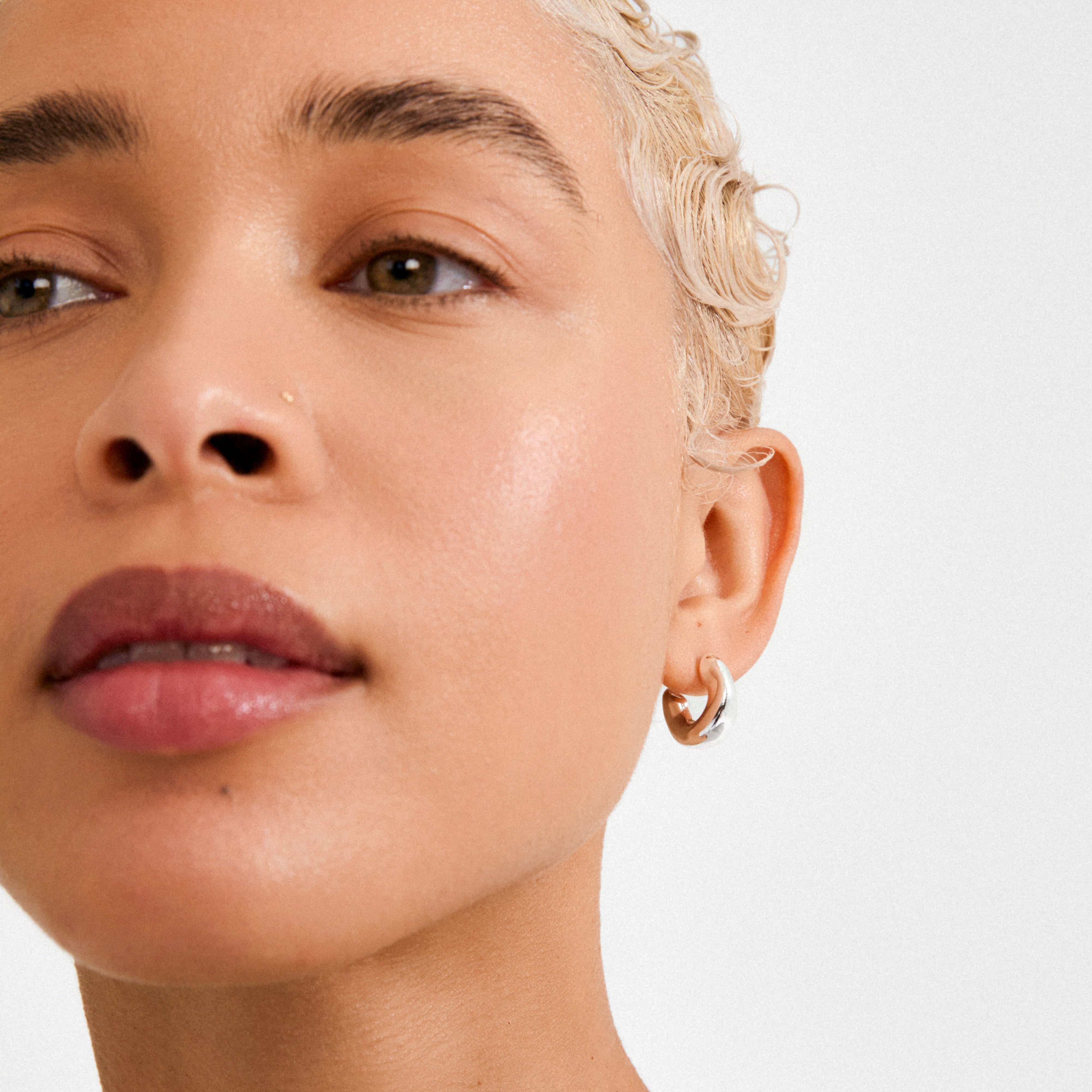Close-up of a person wearing JENNINGS silver-plated mini hoop earring, highlighting its sleek, sculpted design against a minimal, modern look with a smooth complexion.