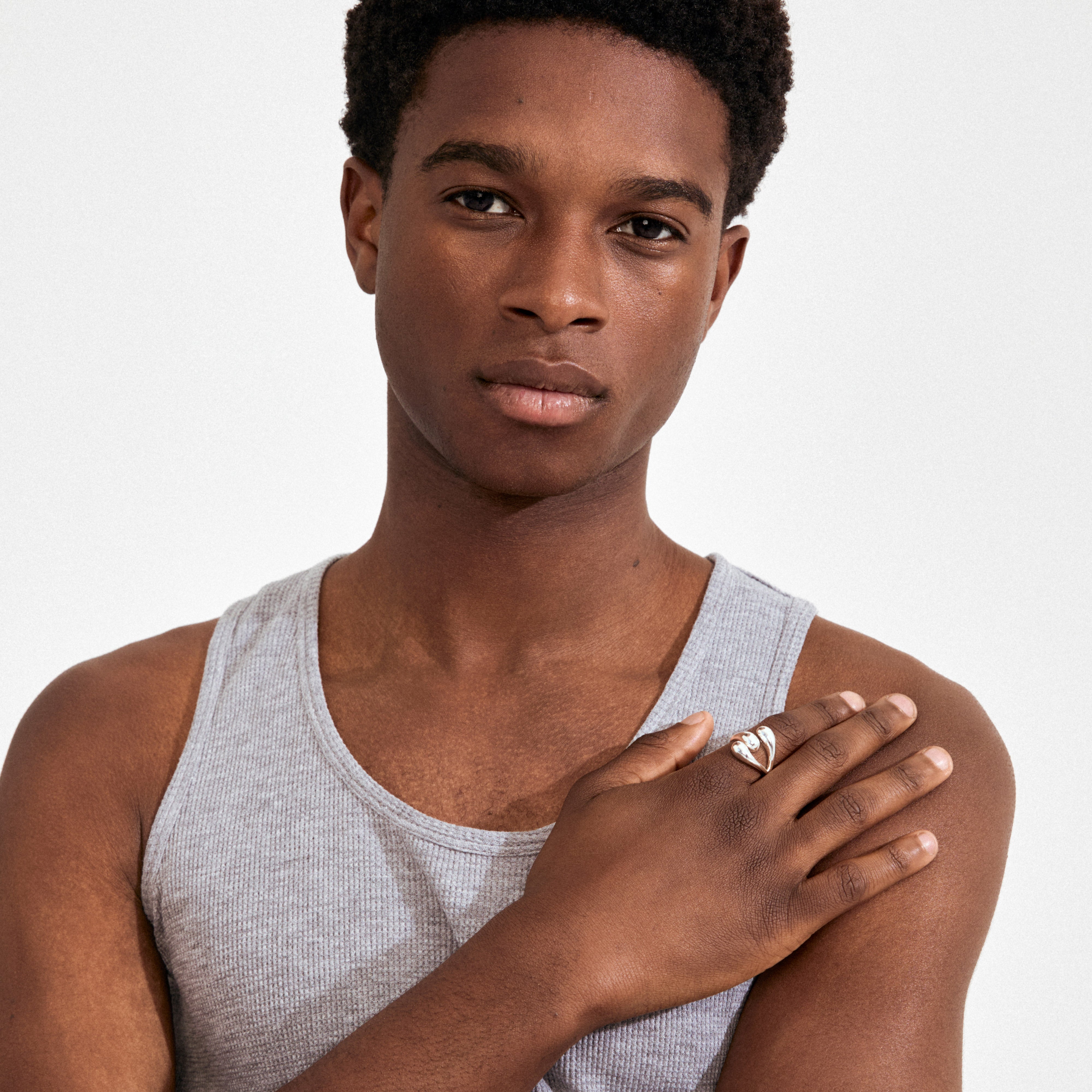 Young person wearing the JENNINGS ring silver-plated, featuring a stylized heart design with a gemstone, on their right middle finger, hand resting on shoulder.