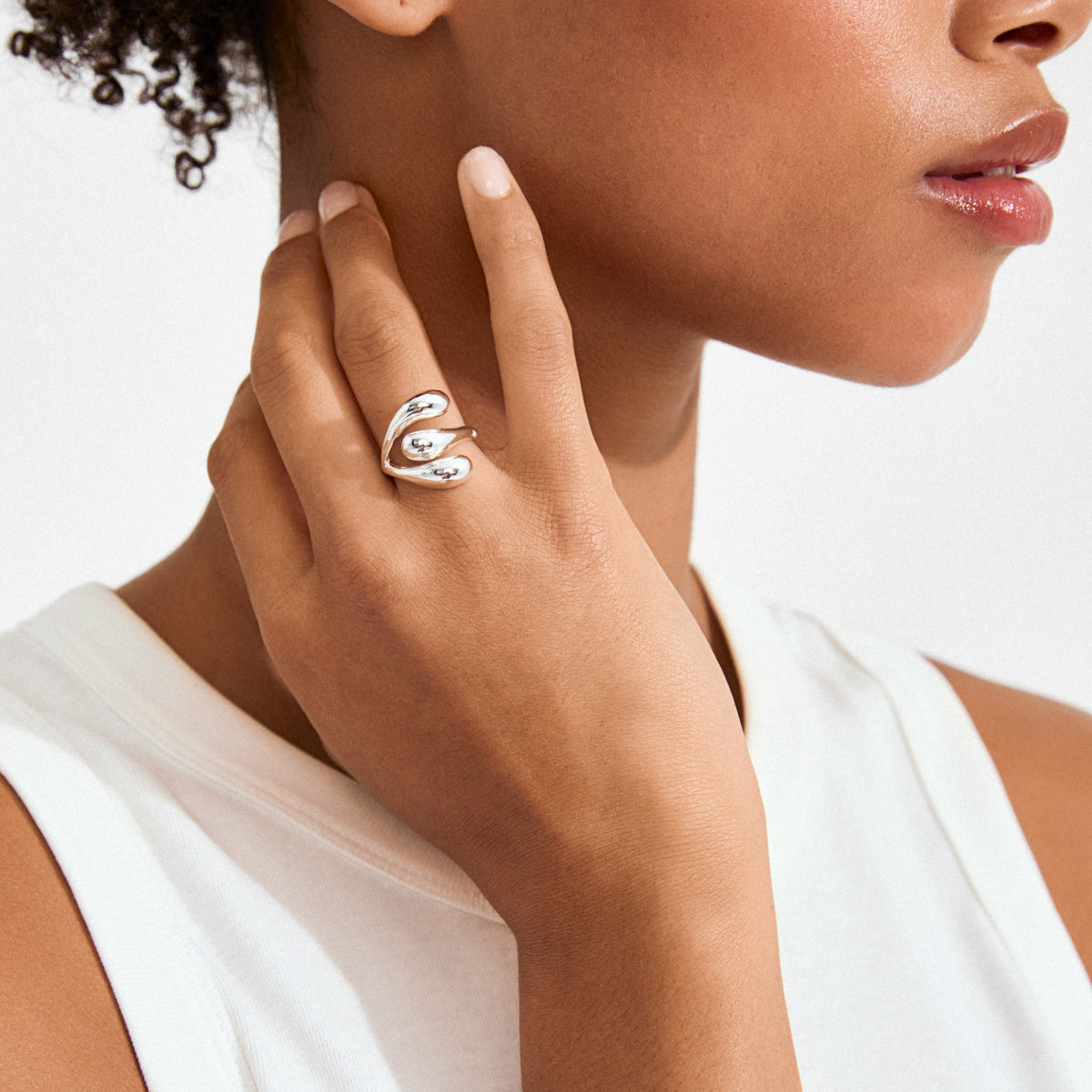 JENNINGS ring silver-plated on finger; sculptural, droplet-like ends wrap elegantly, showcasing its liquid silver design against a white sleeveless top.