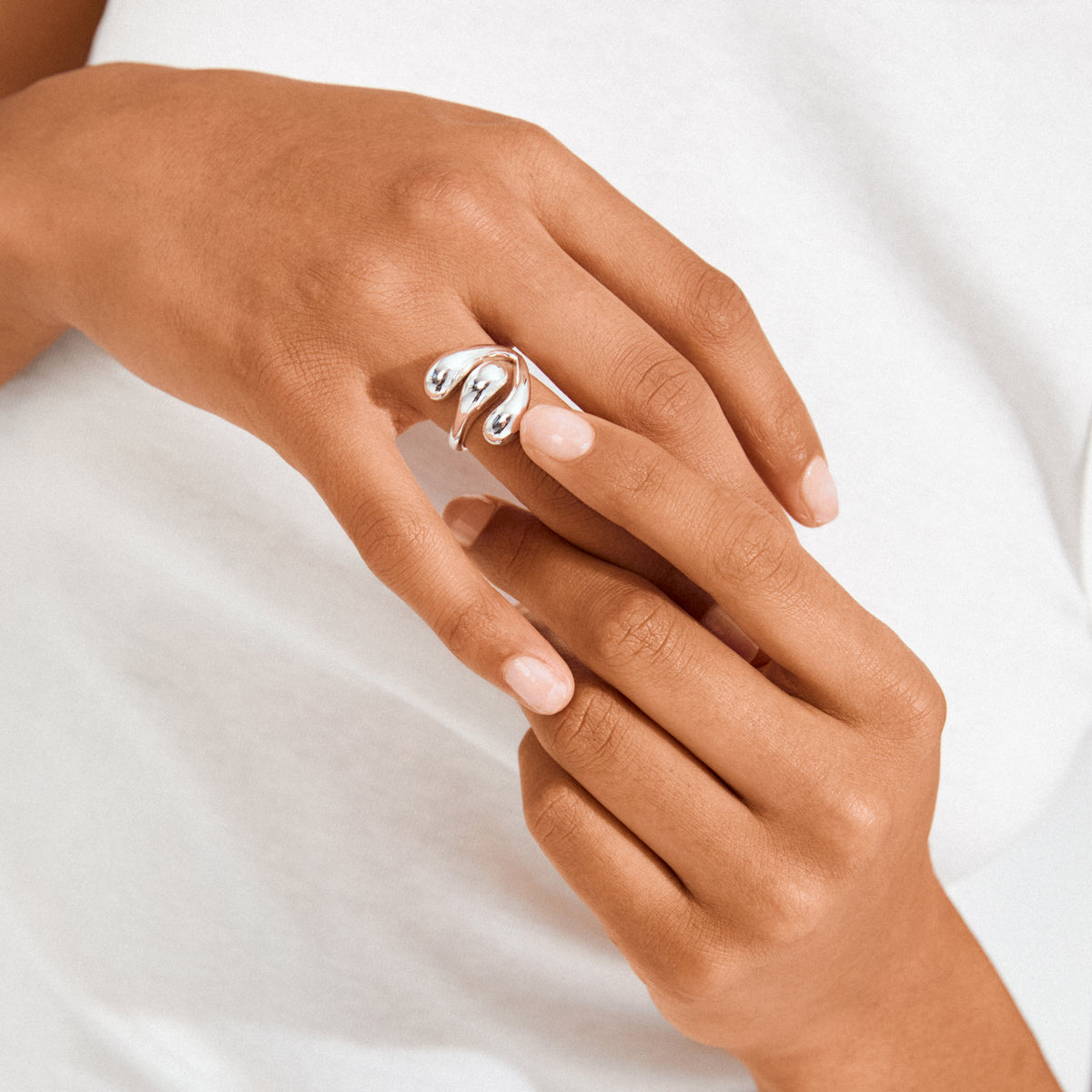 Hands showcasing a silver-plated JENNINGS ring from Pilgrim, featuring a sculptural, melting design with droplet-like forms, exemplifying minimalist style and craftsmanship.