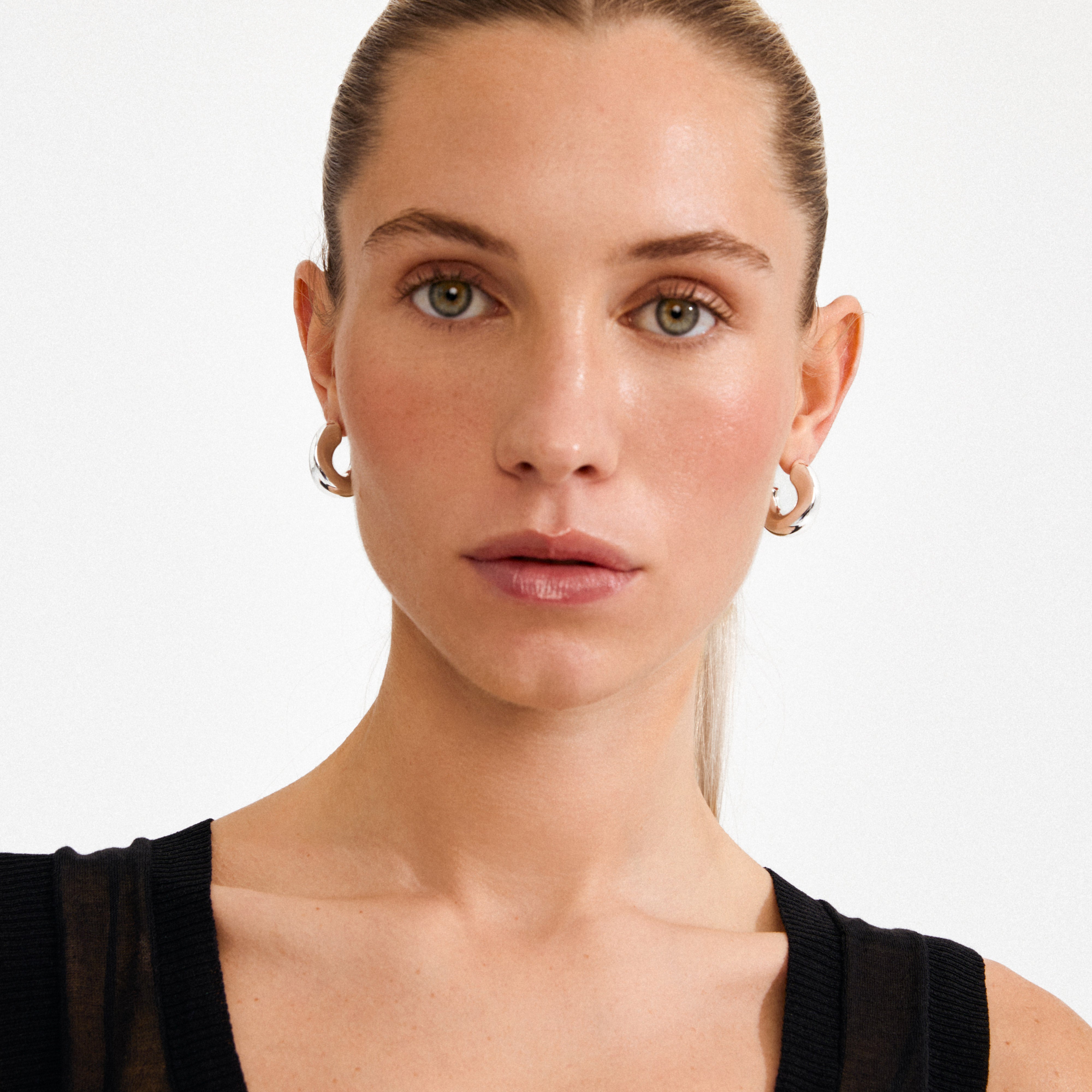 Young woman wearing JENNINGS silver-plated chunky hoop earrings by Pilgrim, showcasing their sculptural, statement-making design against her natural look and minimalist outfit.