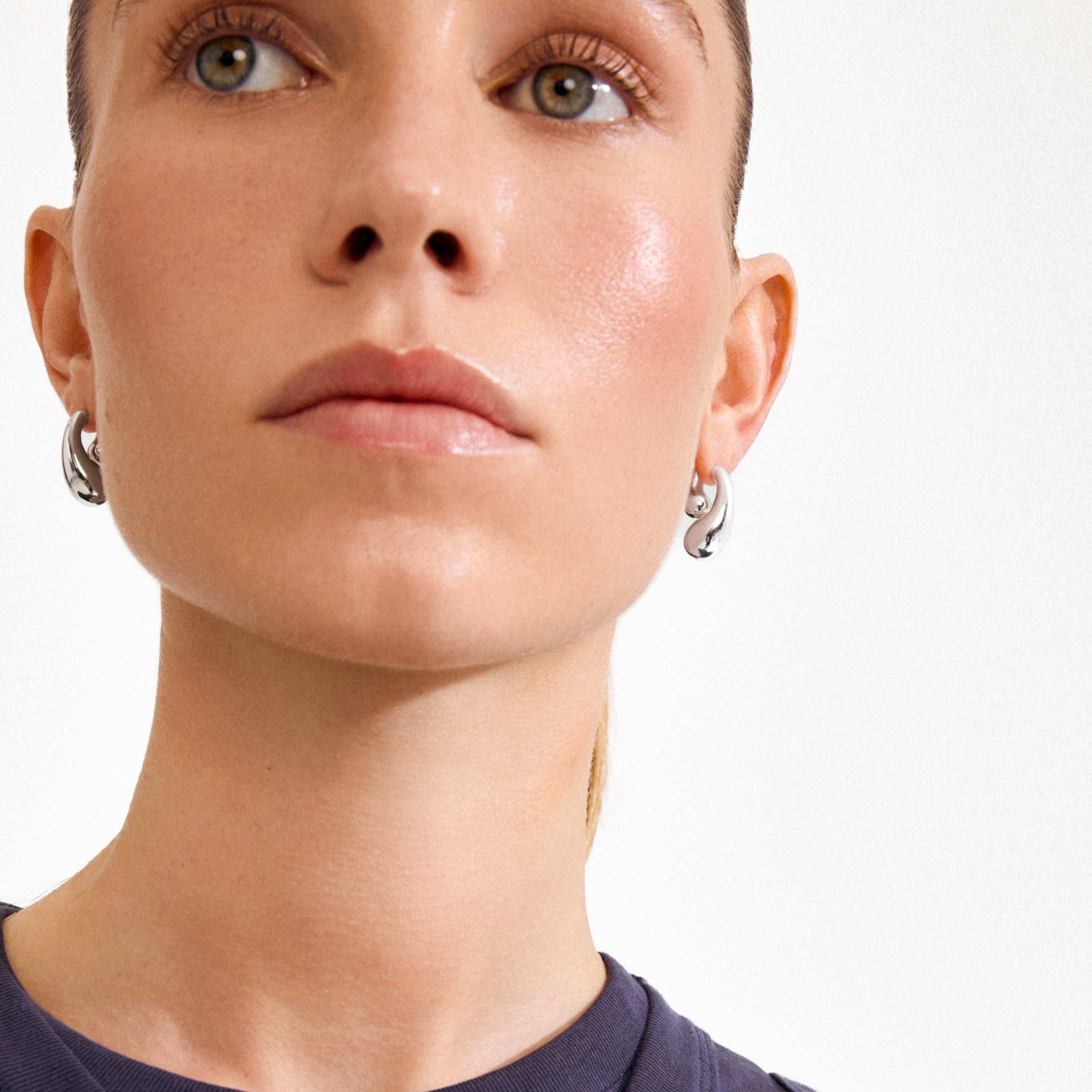 Close-up of a woman wearing the silver-plated JENNINGS earrings by Pilgrim, showcasing their sculptural, twisted hoop design and fluid, melting-drop effect.