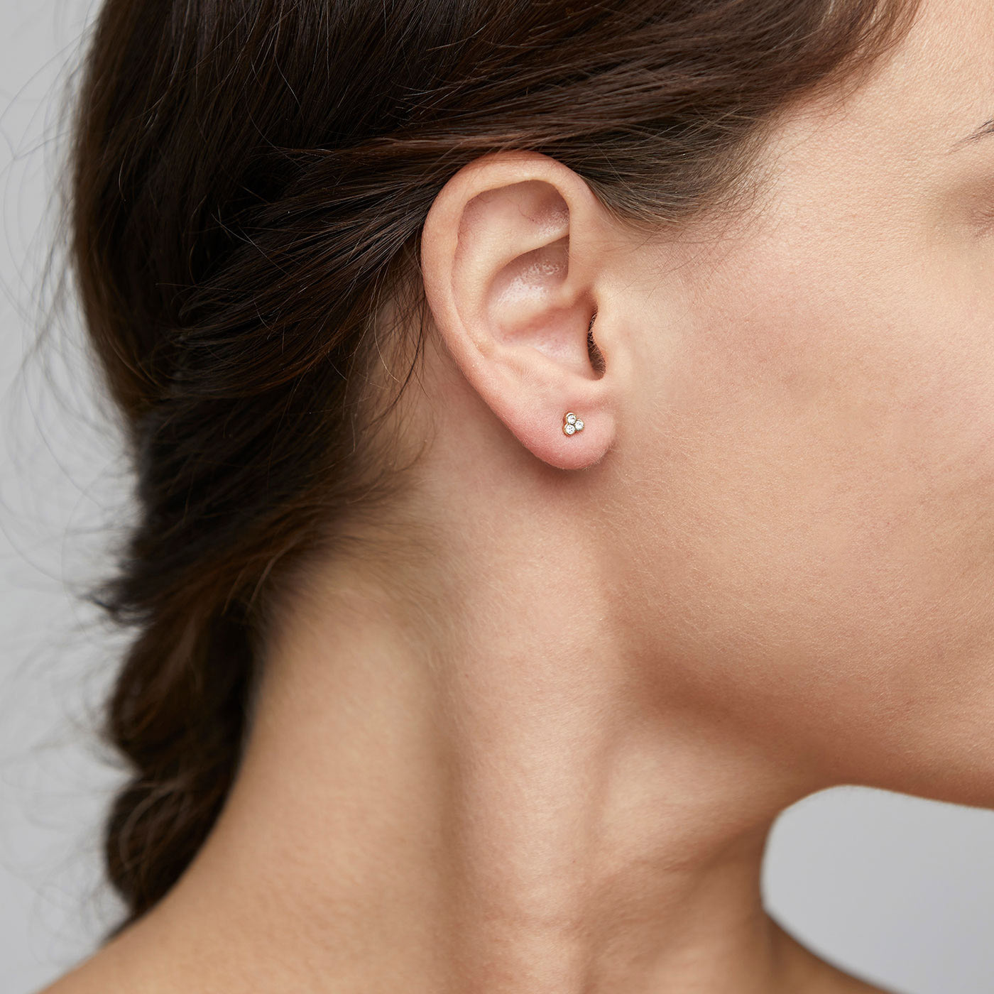 Gold-plated CAILY crystal earrings on a woman's ear, featuring three clear crystals in a bouquet design, embodying elegance and Scandinavian craftsmanship.
