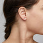 Gold-plated CAILY crystal earrings on a woman's ear, featuring three clear crystals in a bouquet design, embodying elegance and Scandinavian craftsmanship.