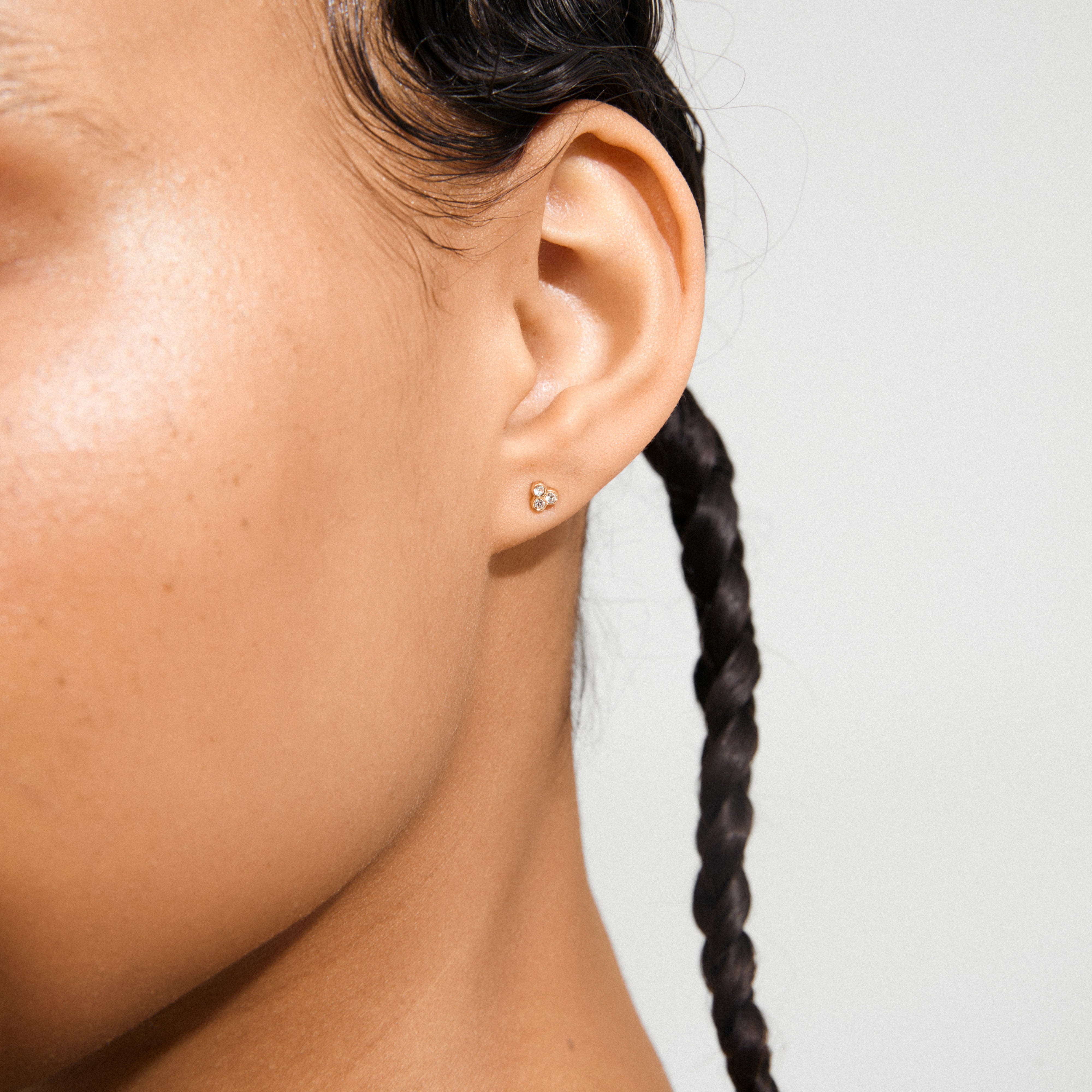 CAILY crystal earrings gold-plated, featuring three tiny stones in a triangular cluster on a pierced ear, embody elegance and subtlety, perfect for complementing feminine outfits.