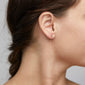 TITIANA gold-plated crystal earrings, featuring three crystals with long chains, elegantly dangle from a woman's ear.