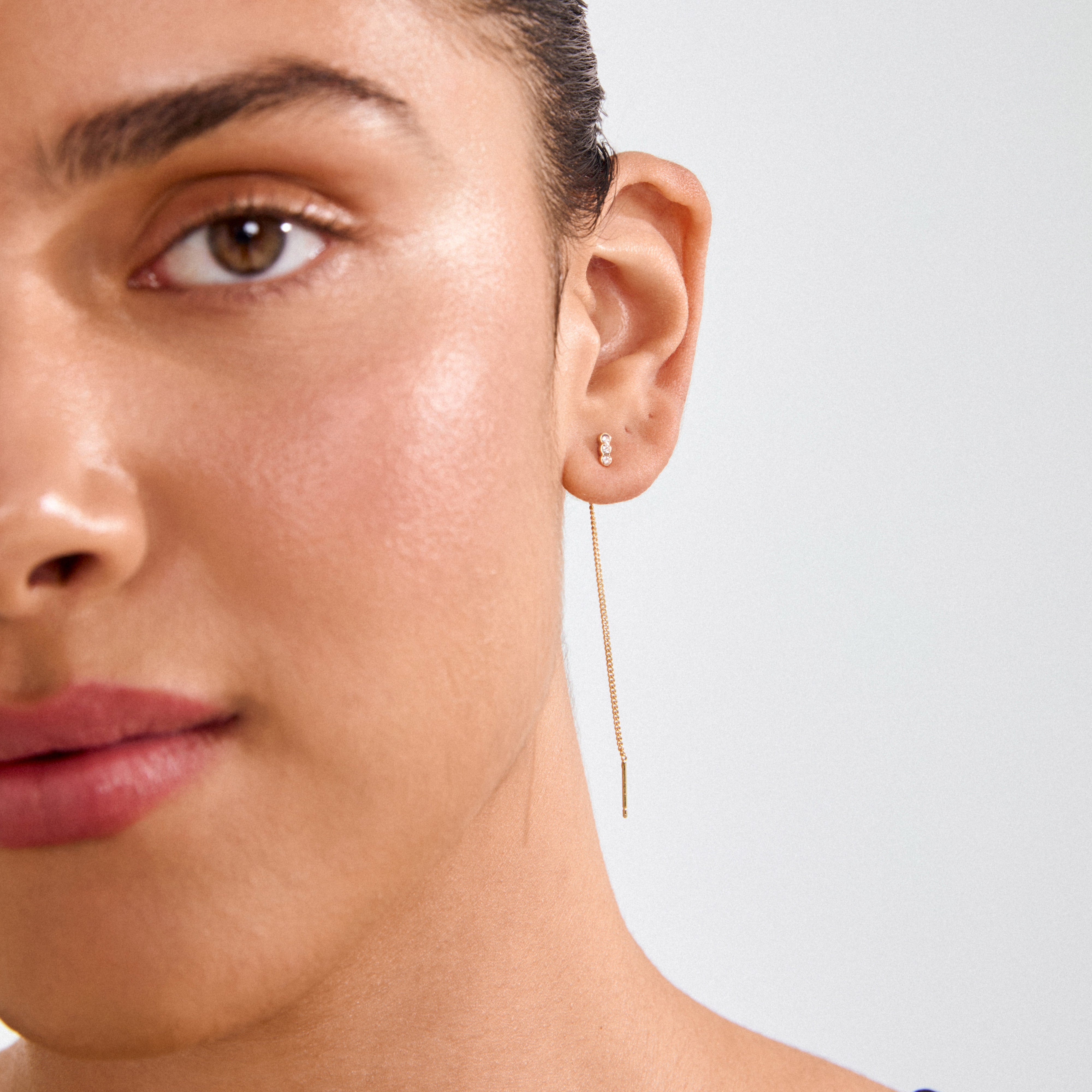 Close-up of a right ear wearing TITIANA crystal earrings gold-plated, showcasing a gold chain threader with Preciosa crystals and a trio-stone stud above.