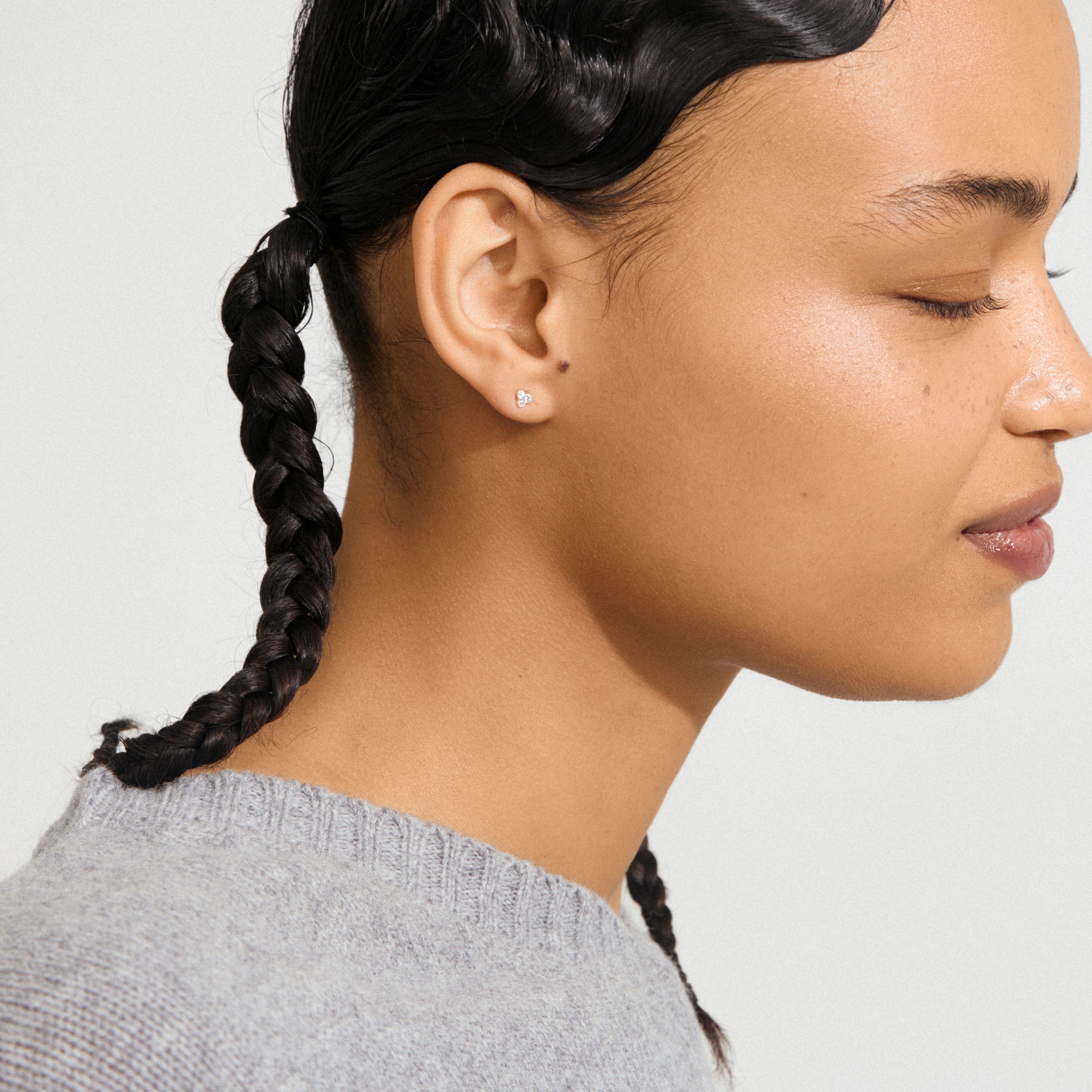 Young woman wearing CAILY crystal earrings silver-plated, featuring three clear crystals in a bouquet design, complementing her neat braid and light gray knit sweater.