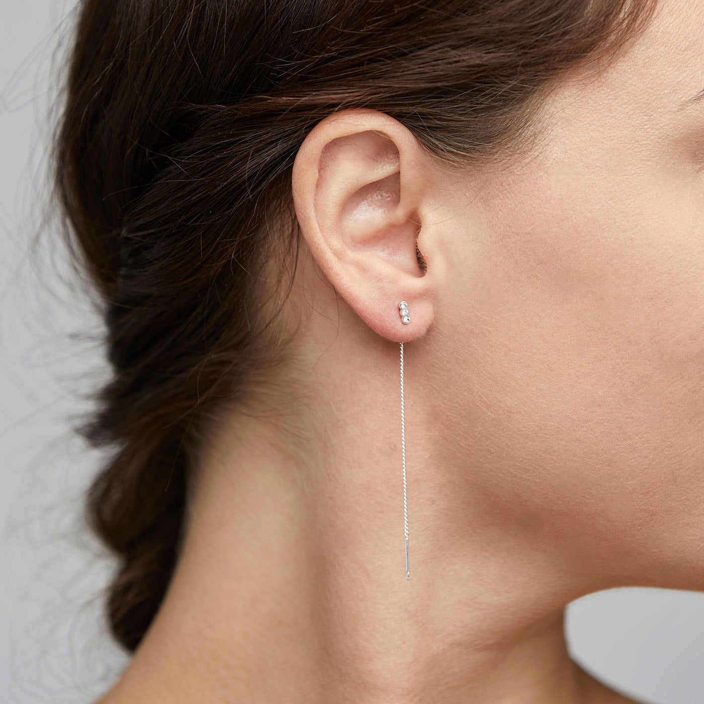 TITIANA crystal earrings, silver-plated, with three clear crystals and delicate chains, elegantly hang from a woman's ear.
