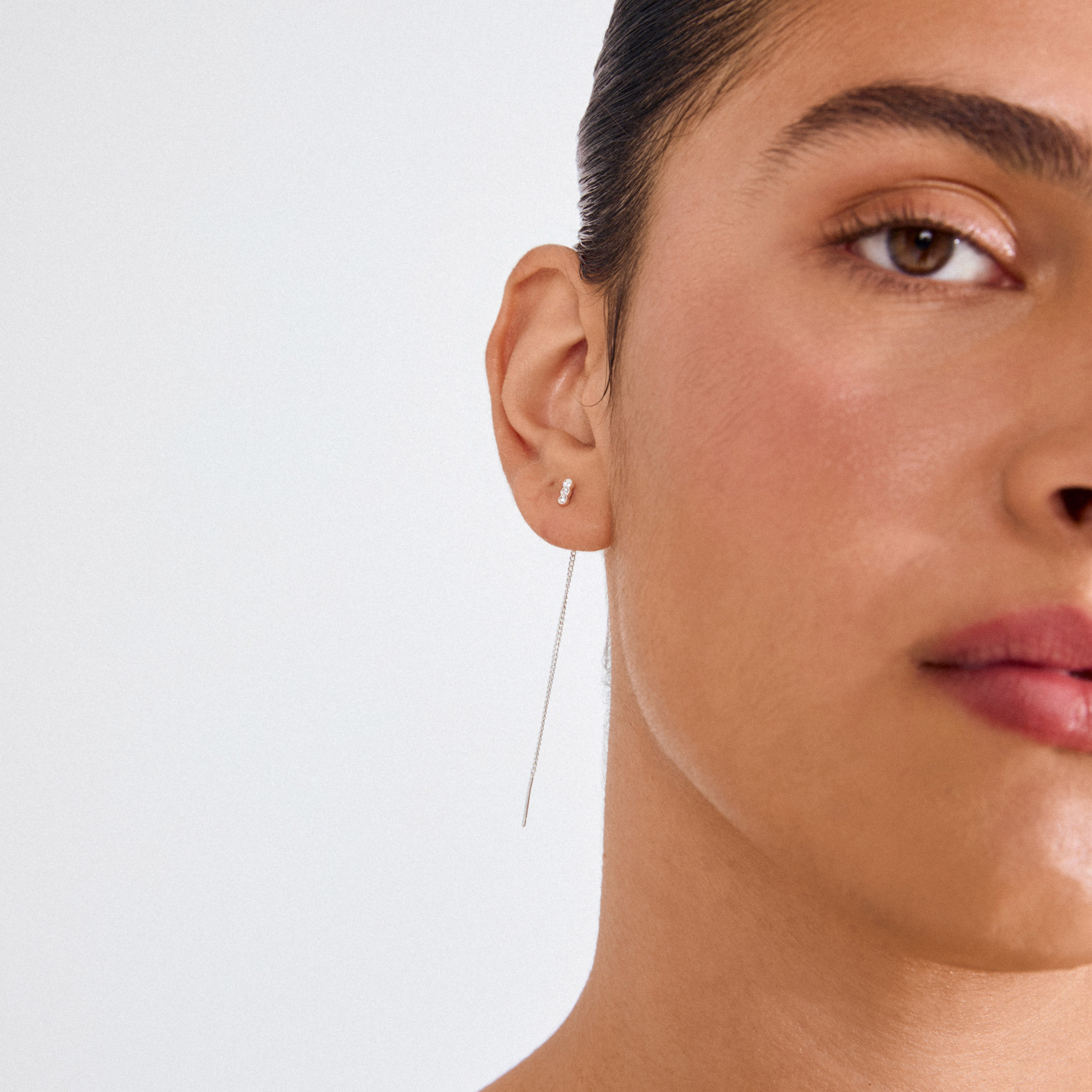 TITIANA crystal earrings silver-plated, showcasing a delicate chain drop and three-stone stud on a woman's ear, embodying elegance and movement with recycled craftsmanship.