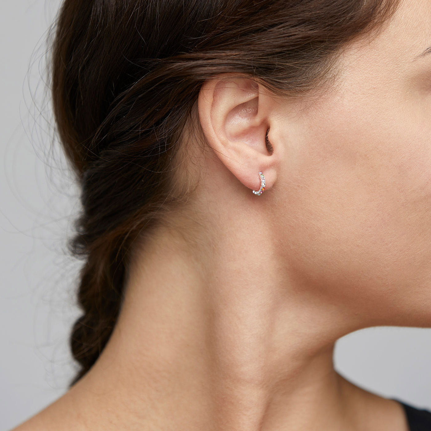 BRIGITTE multicolored crystal half hoops silver-plated adorn a woman's ear, showcasing sparkling crystals and a fine, undulating edge capturing light elegantly.