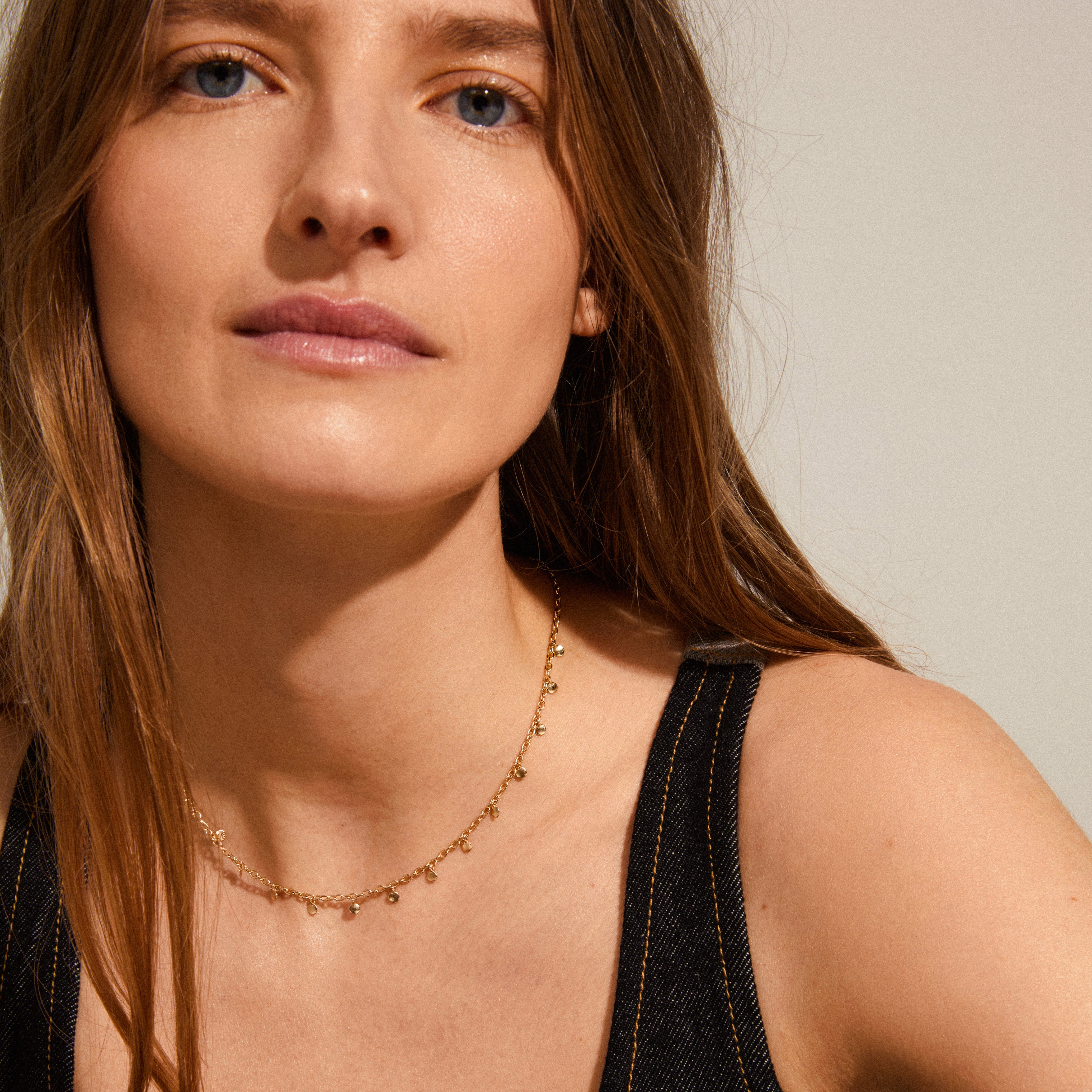 PANNA coin necklace gold-plated elegantly draped on a woman with long hair, showcasing small round polished pendants, embodying both classic and edgy style.