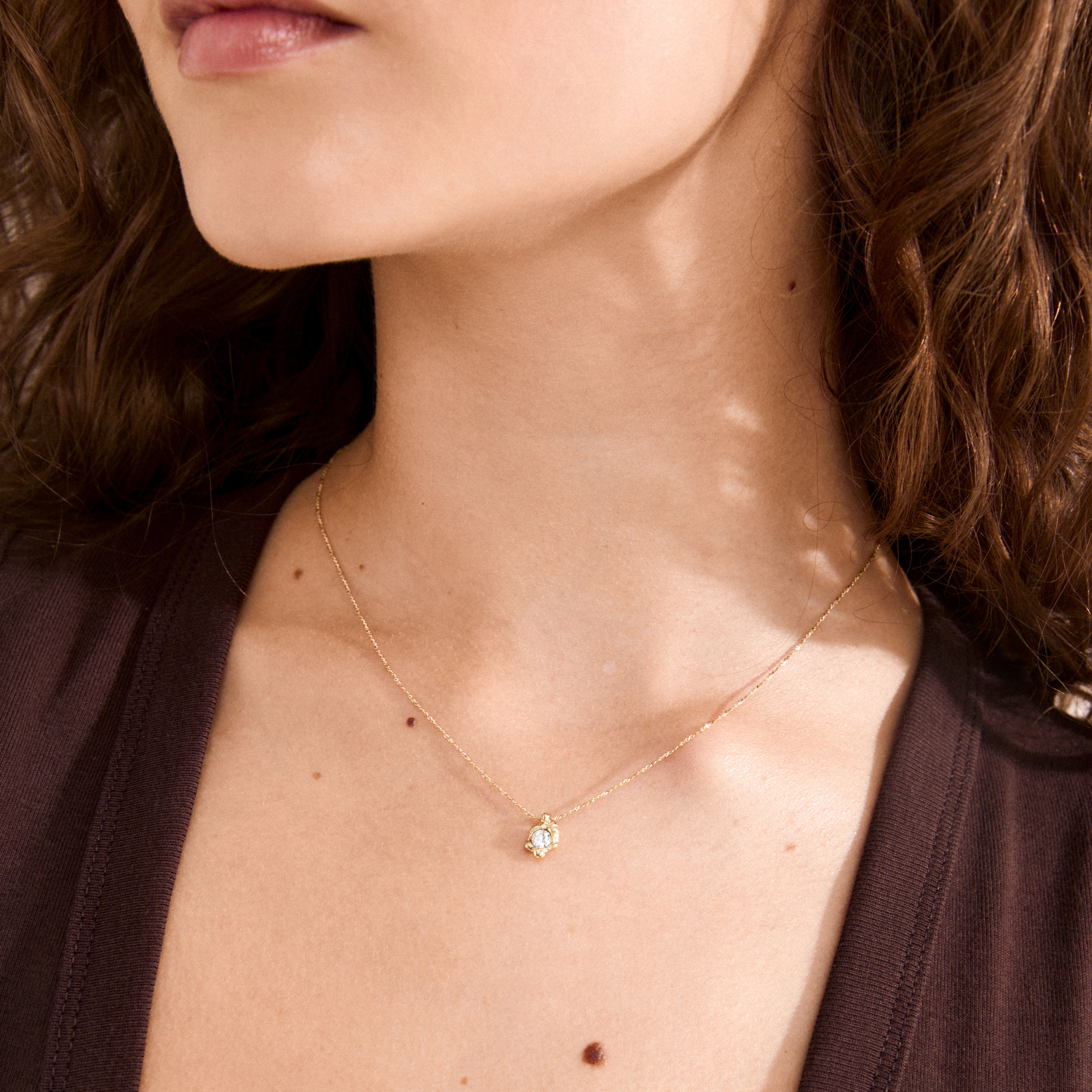 Woman wearing the TINA crystal pendant necklace gold-plated, showcasing a delicate gold chain with an asymmetrical pendant featuring a sparkling crystal.