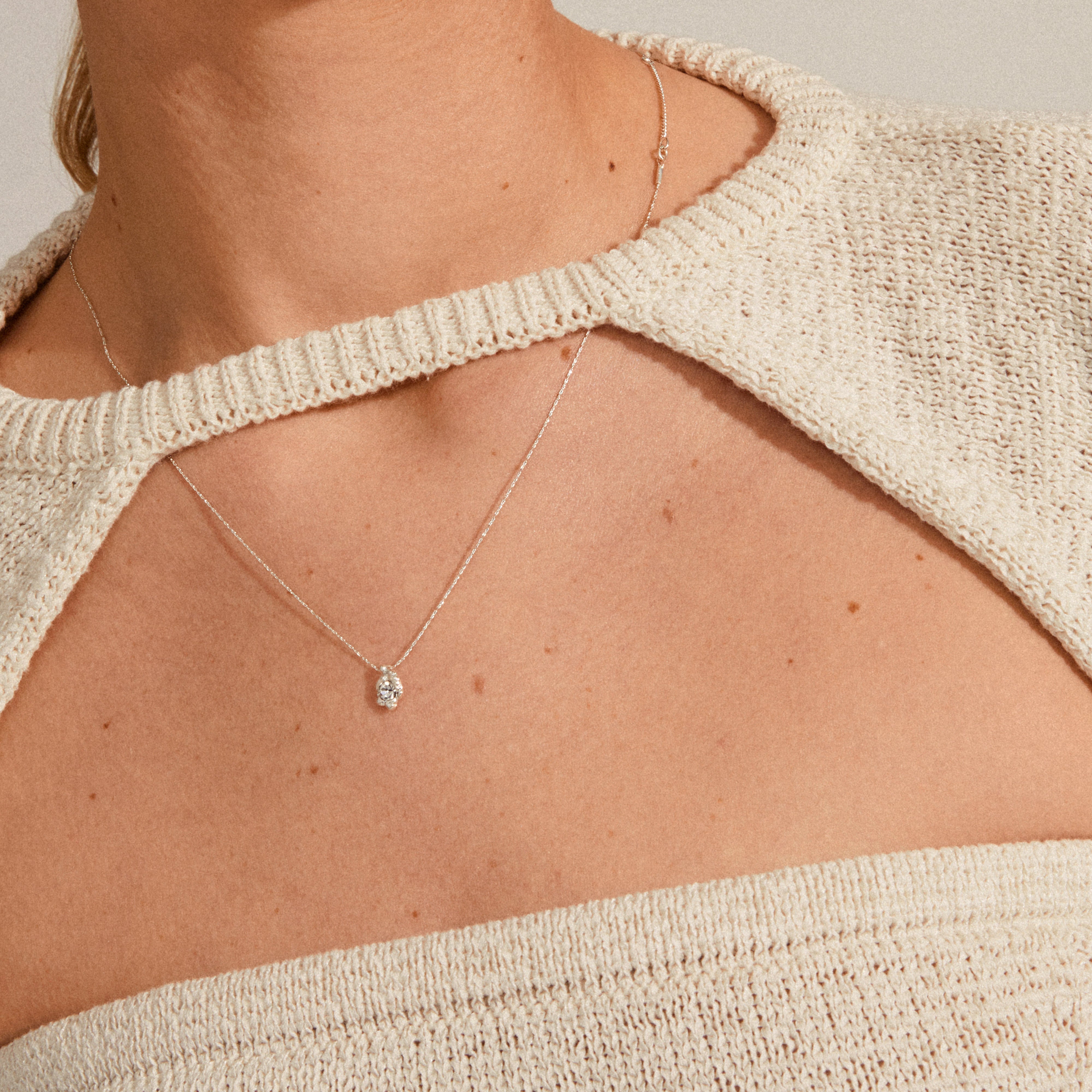 TINA crystal pendant necklace, silver-plated, elegantly rests on a knit top, showcasing a delicate round gemstone, embodying Pilgrim's blend of nature-inspired design and recycled craftsmanship.