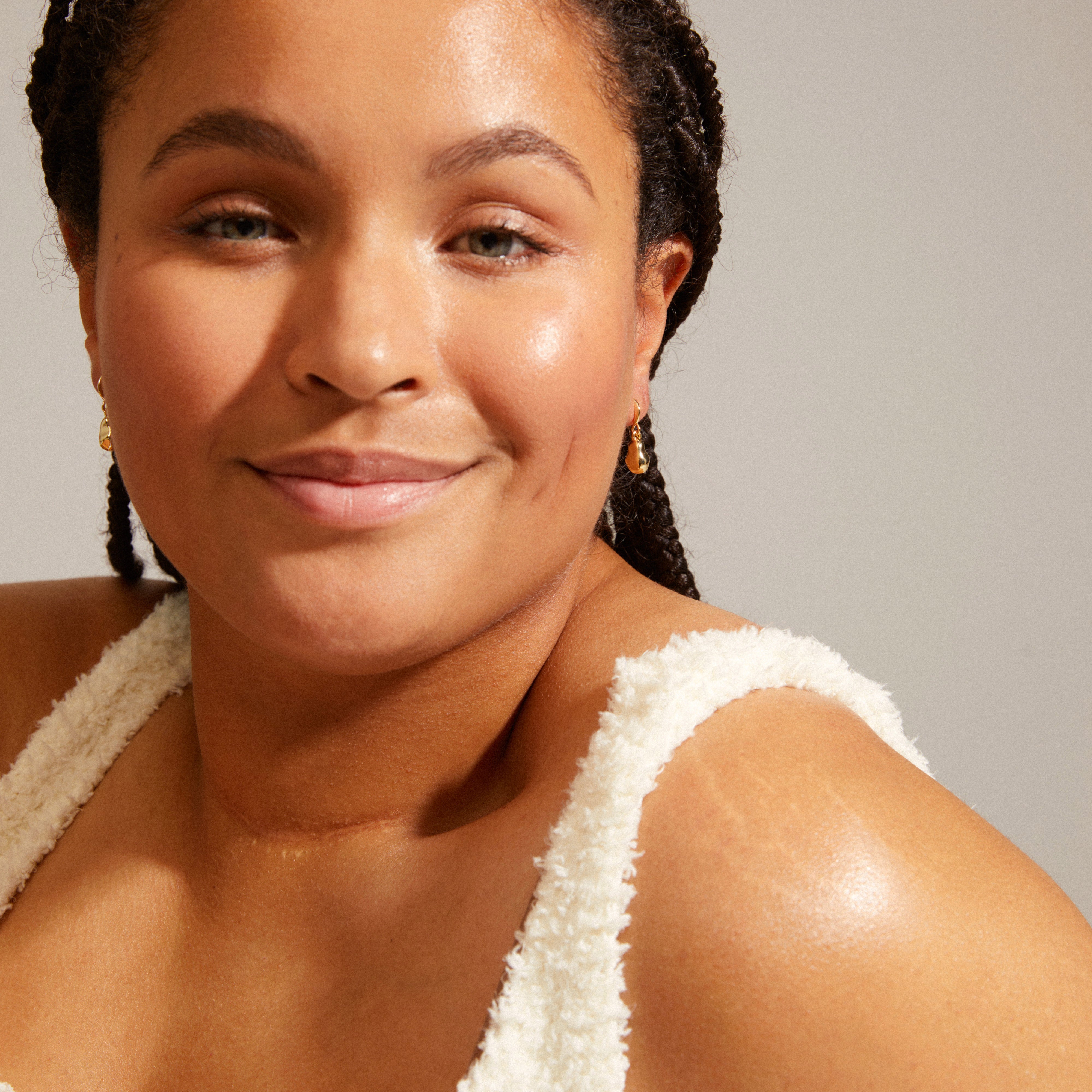 Smiling woman wearing Pilgrim's CHANTAL gold-plated earrings, showcasing organic shapes and shiny surfaces, embodying nature's imperfections and recycled craftsmanship.