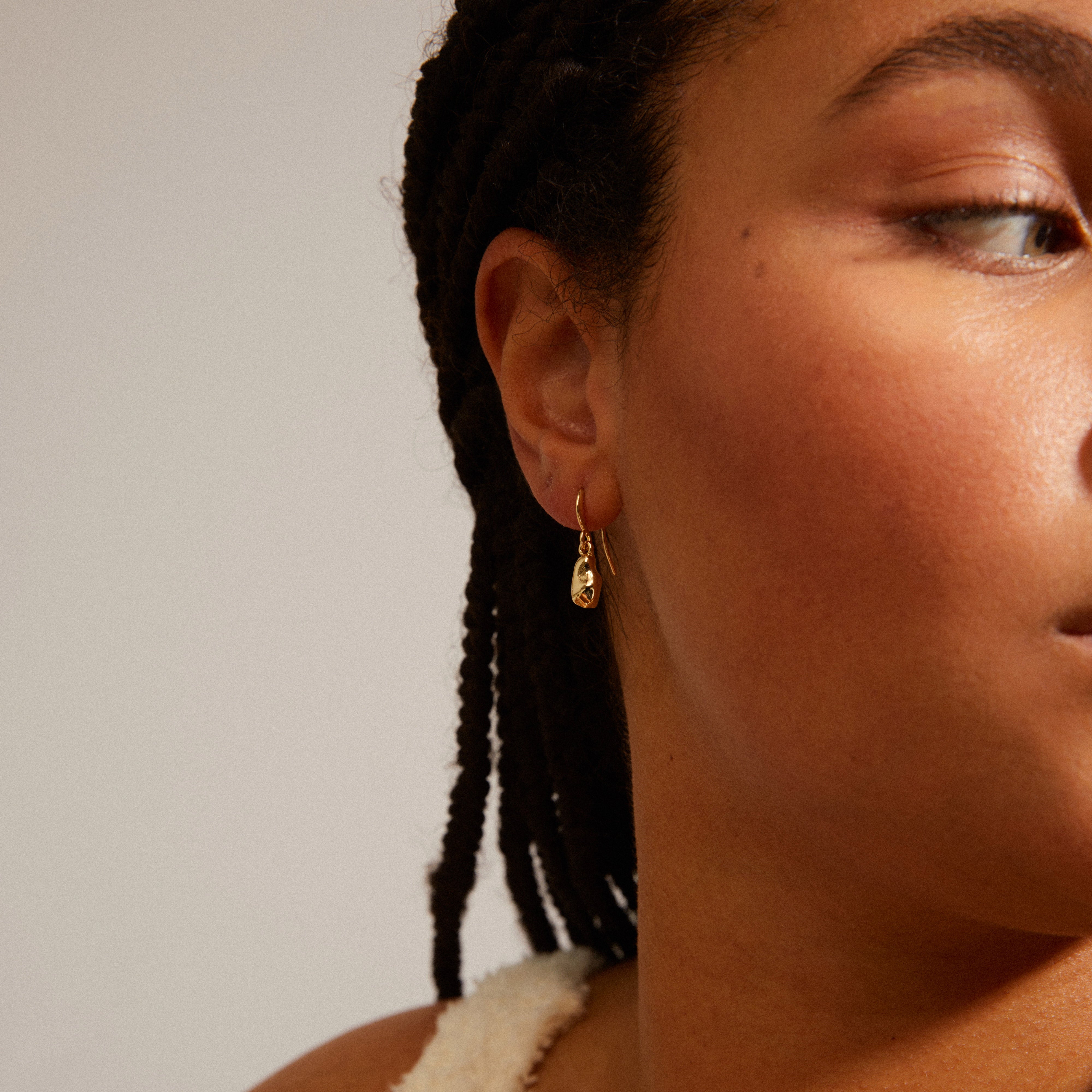 Close-up of a woman wearing Pilgrim's CHANTAL gold-plated earrings, showcasing their organic, shiny design made from 99% recycled materials, inspired by nature's imperfections.