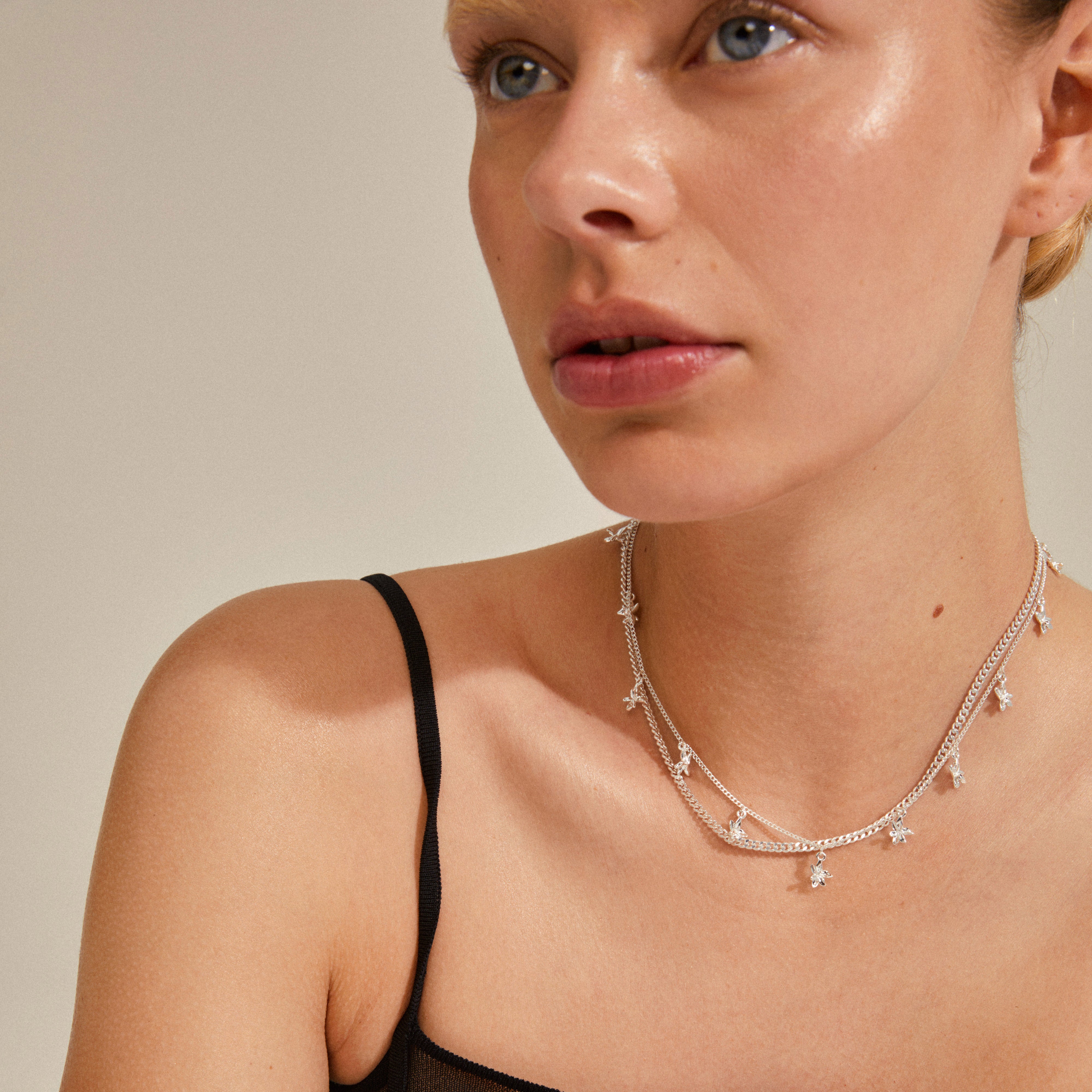 Woman wearing RIKO necklaces, a 2-in-1 silver-plated set by Pilgrim, featuring a layered slim curb chain and nature-inspired flower pendants.