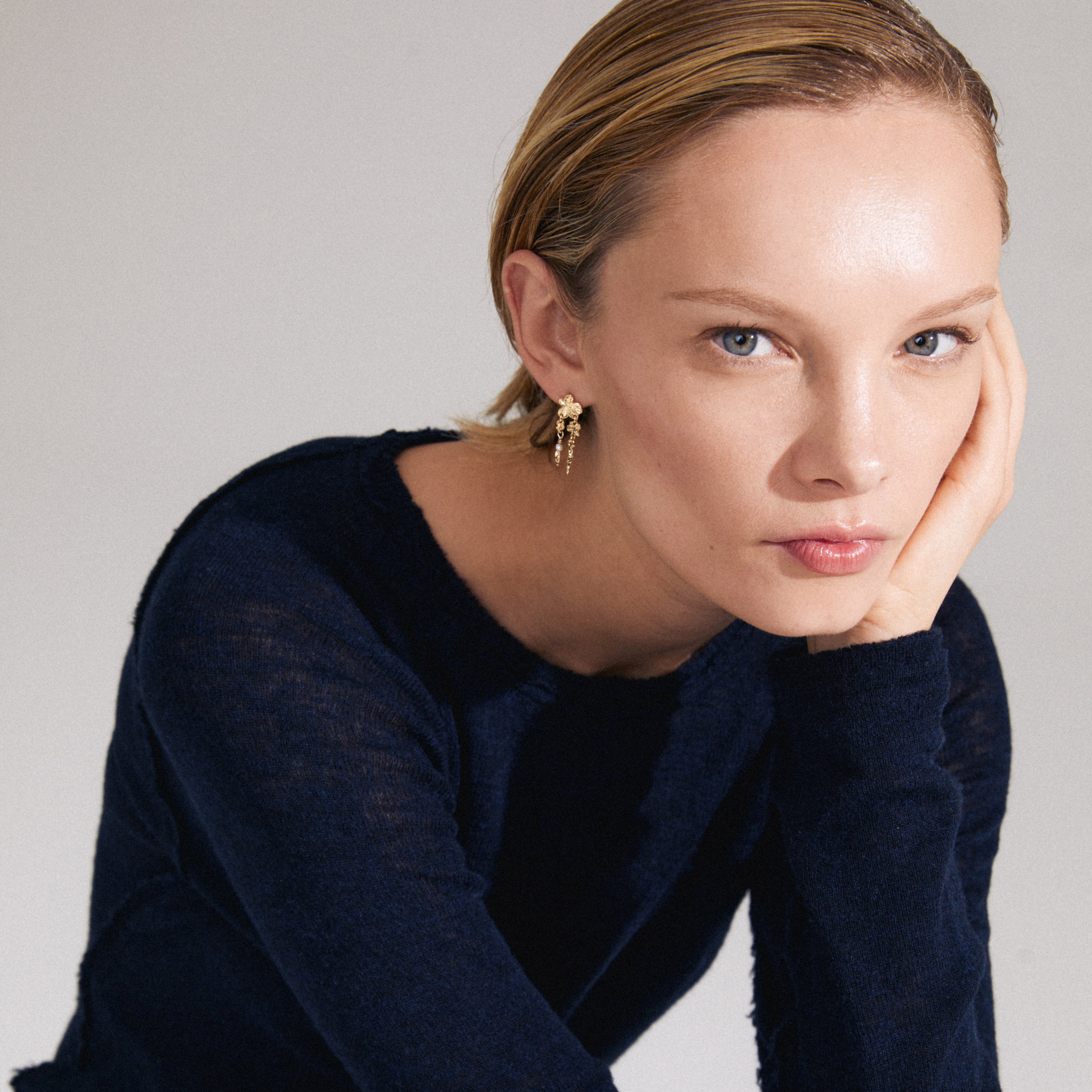 ZHURI gold-plated earrings with delicate floral motifs and a freshwater pearl, showcased by a woman gently touching her face, highlighting their romantic elegance.