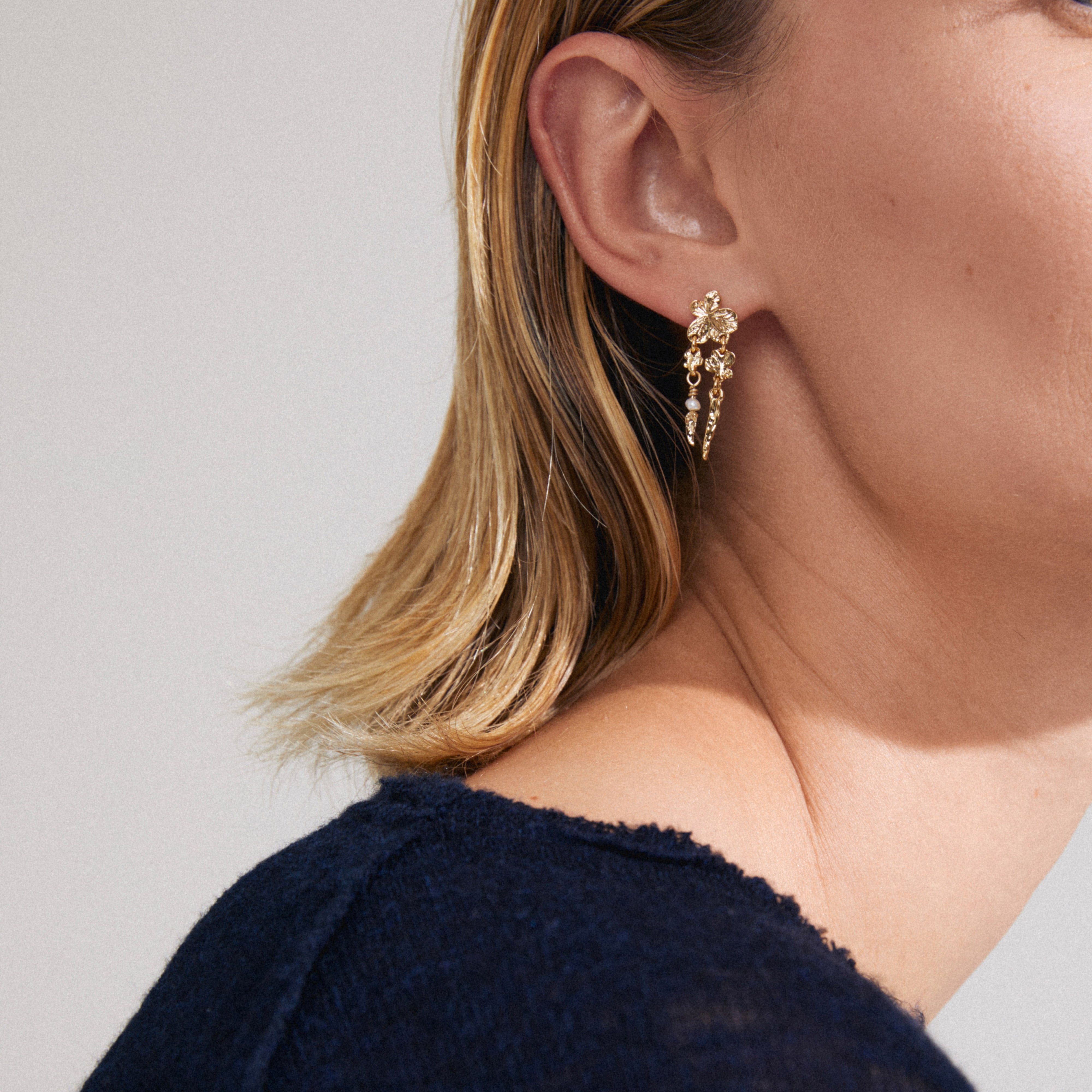 ZHURI earrings gold-plated with floral motifs and delicate chains, worn by a person with short hair, showcasing a romantic, playful design perfect for any occasion.