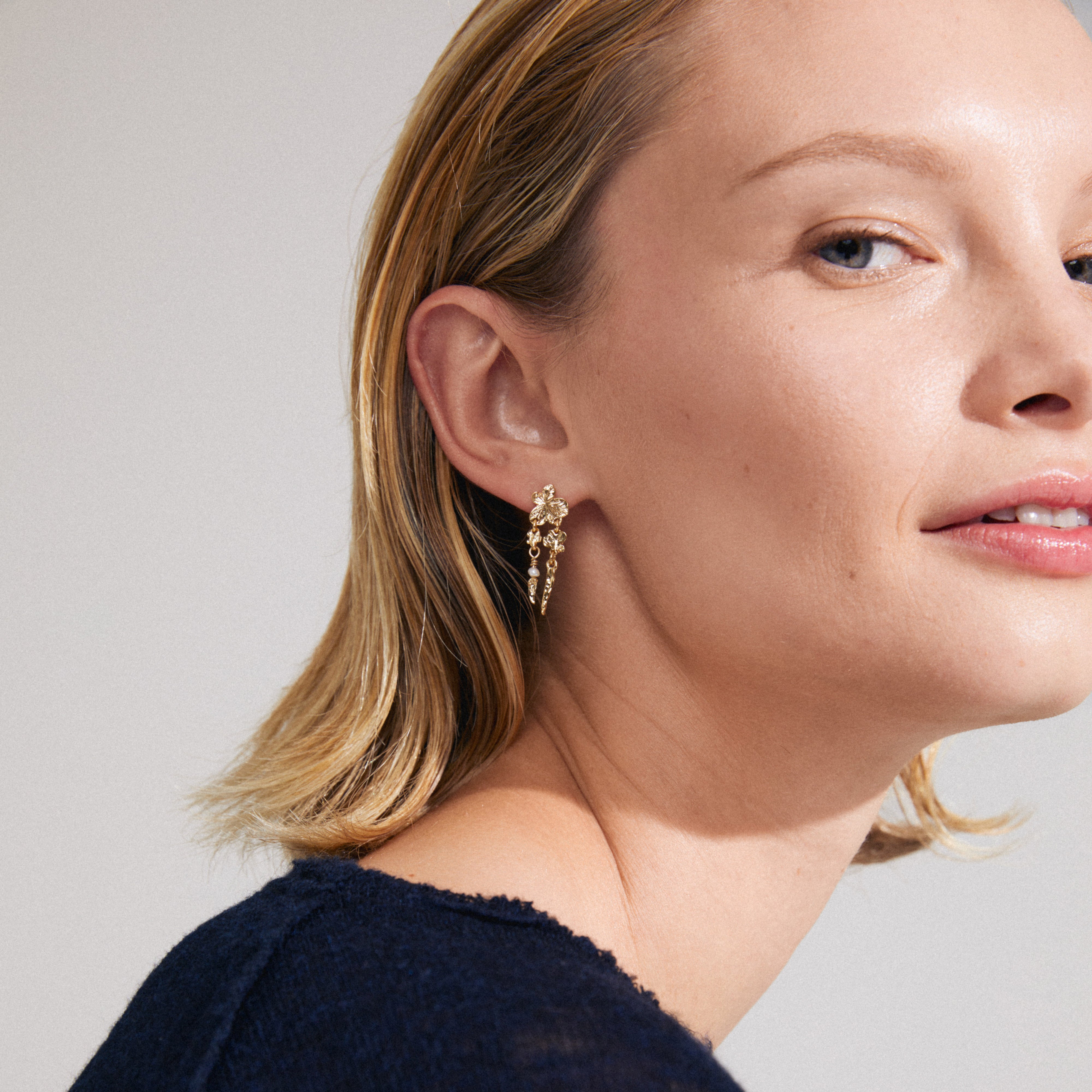 Gold-plated ZHURI earrings featuring delicate floral motifs and a petite freshwater pearl, crafted from 97% recycled materials for an elegant, playful style.