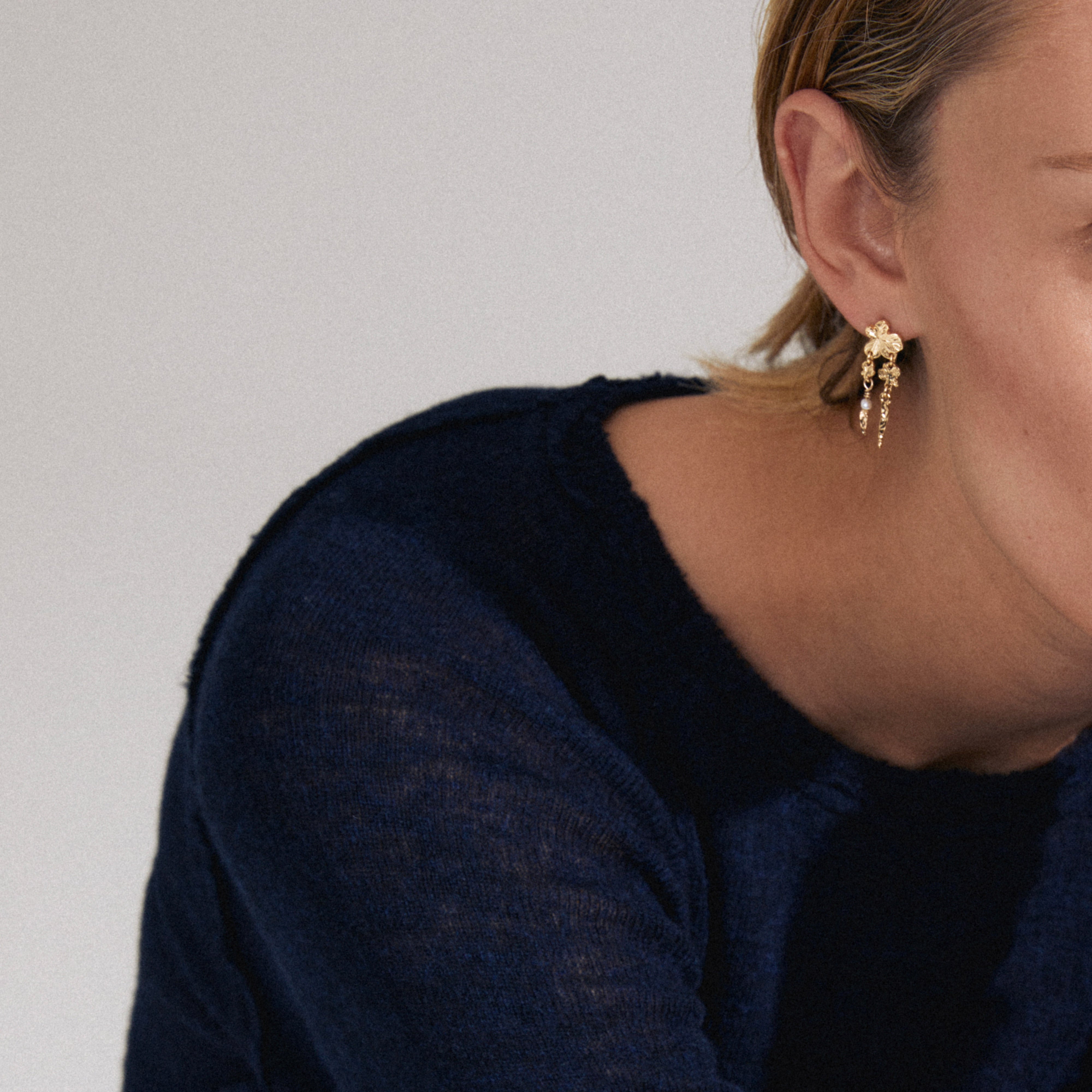 Close-up of a person wearing gold-plated ZHURI earrings featuring delicate floral motifs and a freshwater pearl, highlighting their vibrant, playful elegance for versatile style.