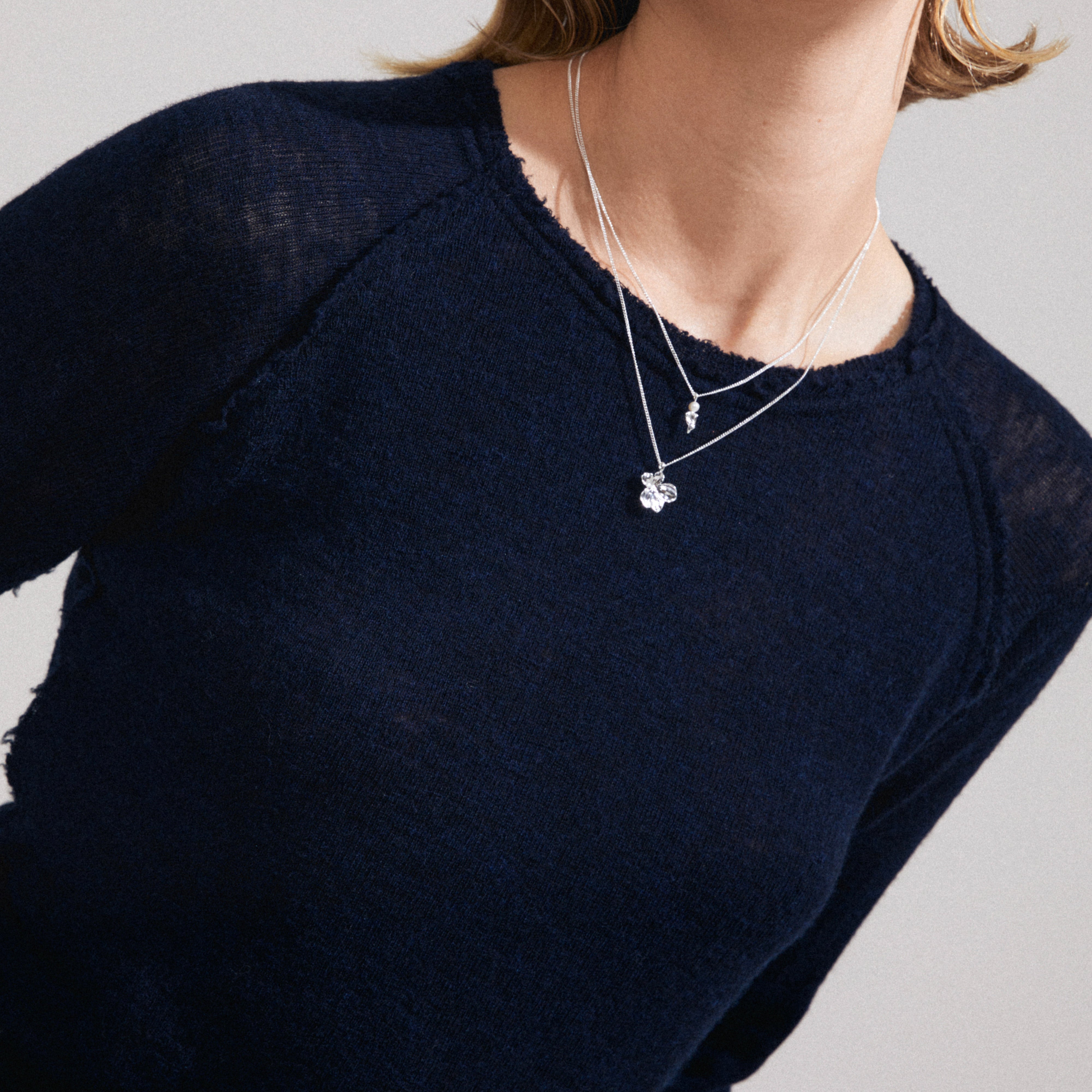 ZHURI necklace 2-in-1 set silver-plated, featuring a four-leaf charm and pearl cluster pendant, layered on a dark navy knit top.